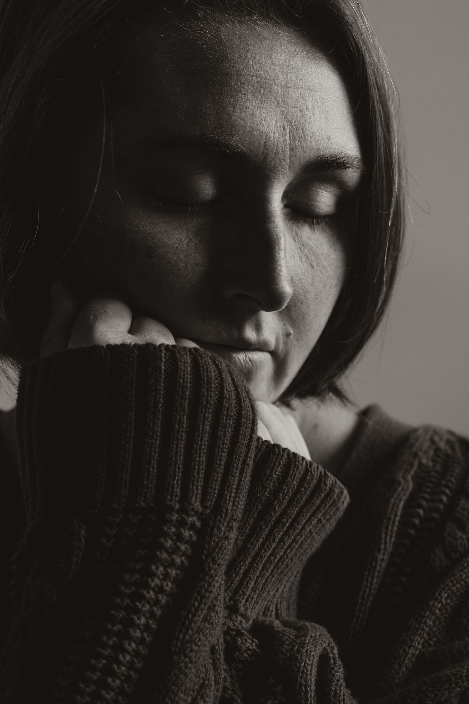 Dramatic black and white portrait of a female figure in a knit sweater with dark shadows and soft lighting.