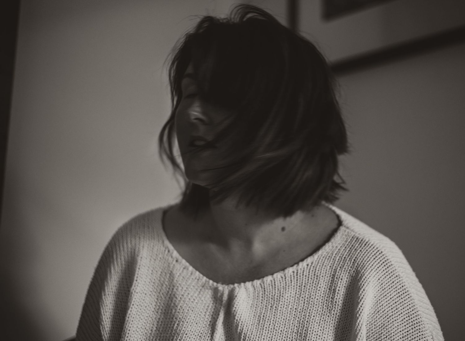 A dark, moody black and white portrait of someone in a light sweater looking down pensively.