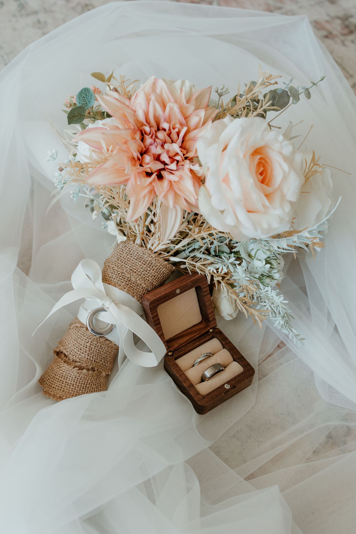 Wedding details featuring peach flowers, burlap accents, and wedding rings in a wooden box.