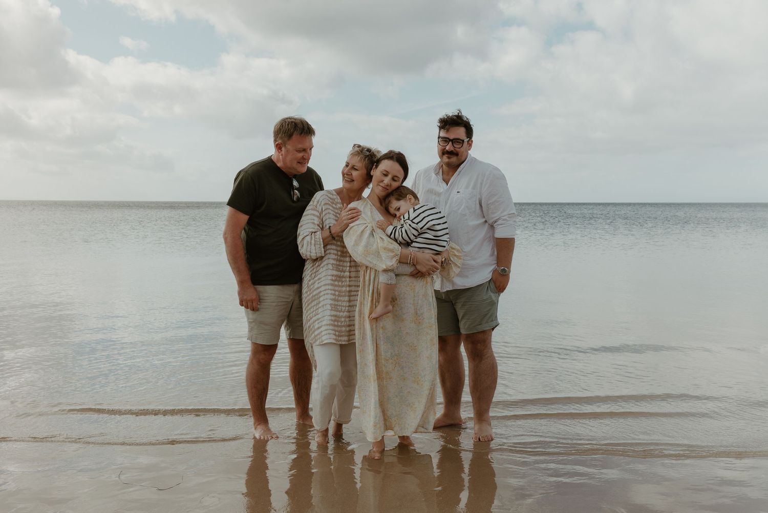 A family portrait on a sunny beach with calm ocean waters in the background.