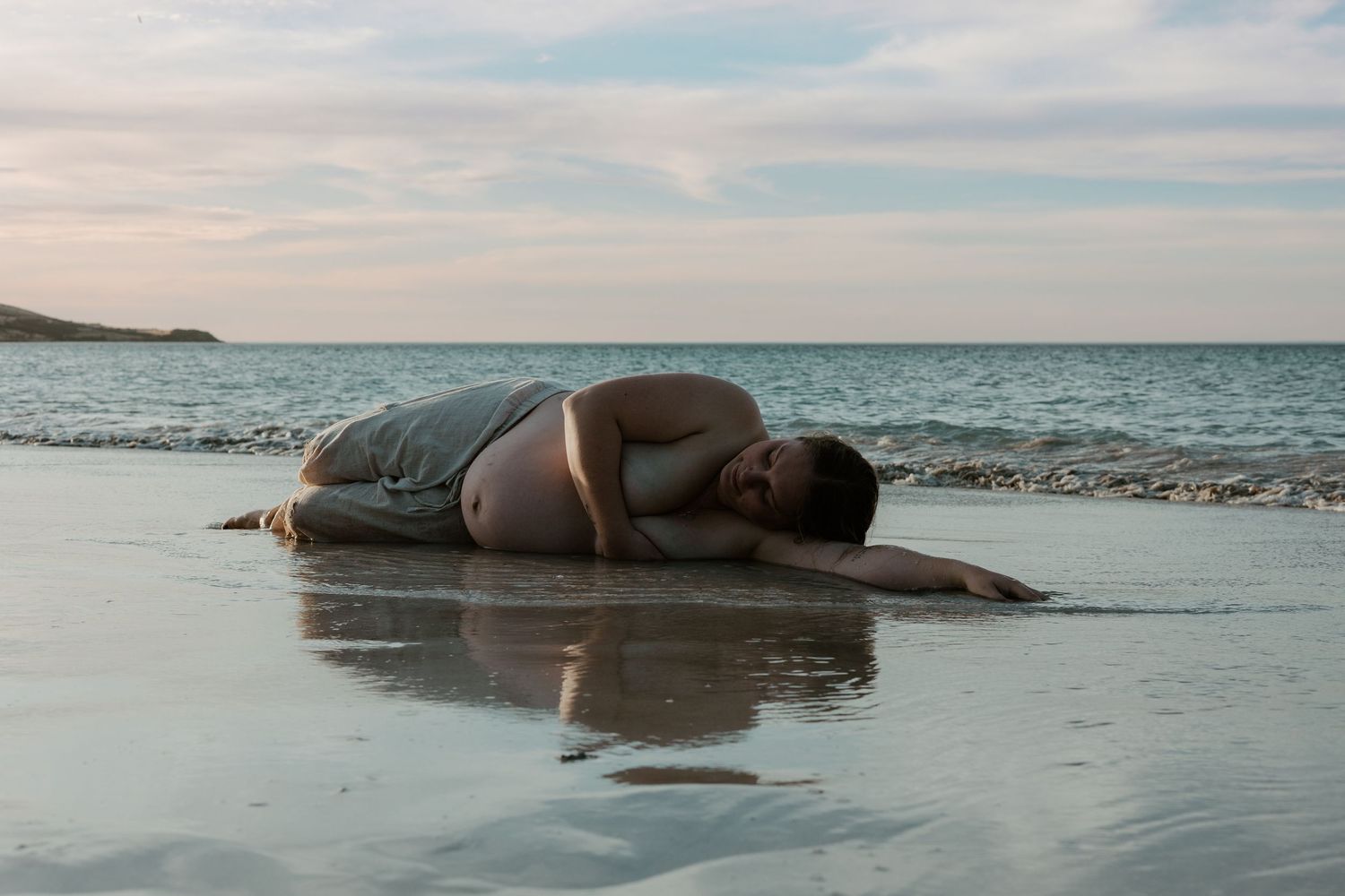 Person lying peacefully on wet sand at the beach during sunset.