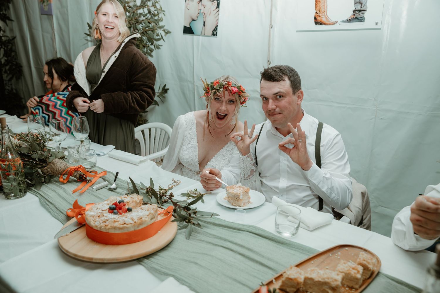A newlywed couple reacts with joy while seated at their wedding reception table.