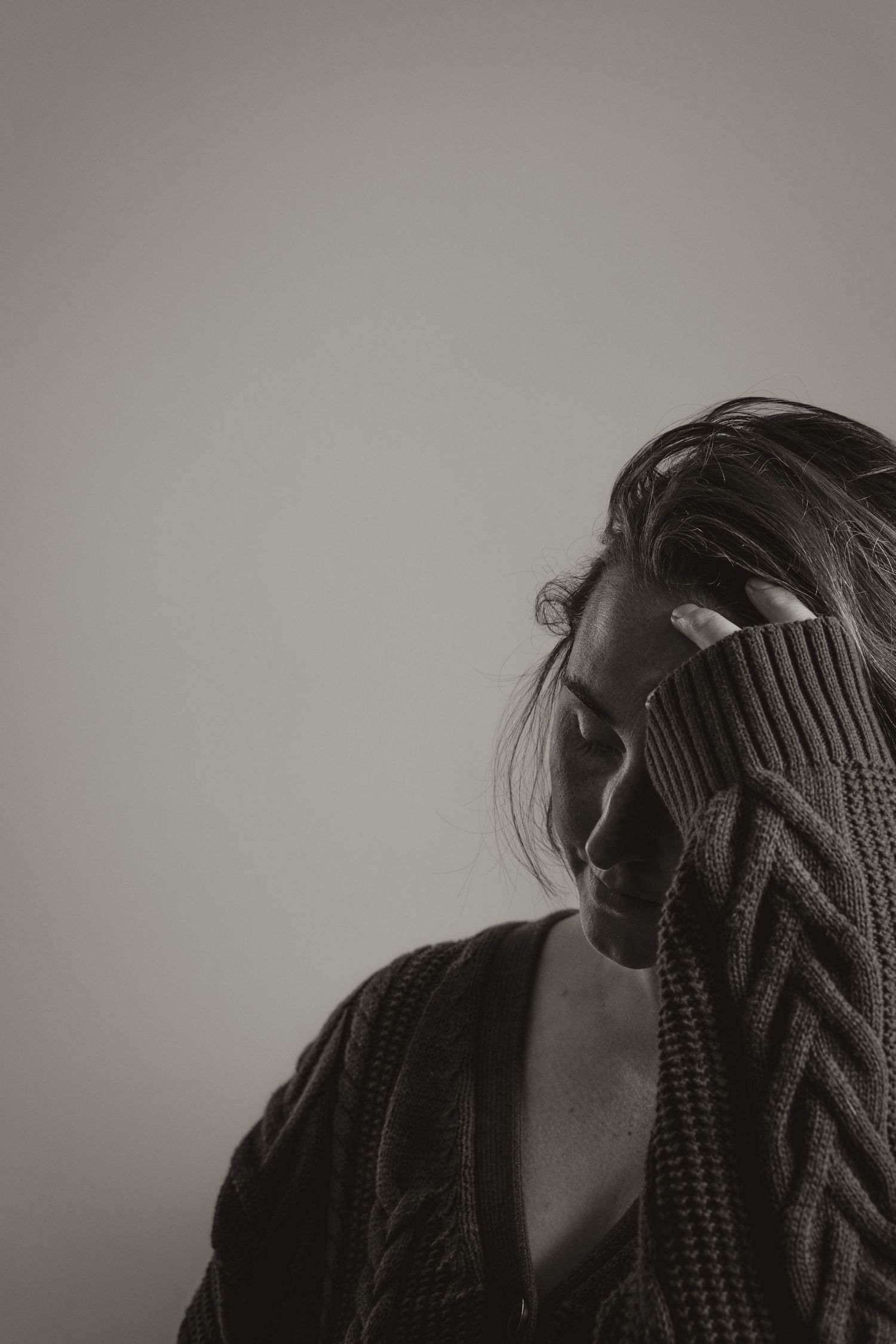 A moody black and white portrait composition showing a figure in a knit sweater with dramatic side lighting.