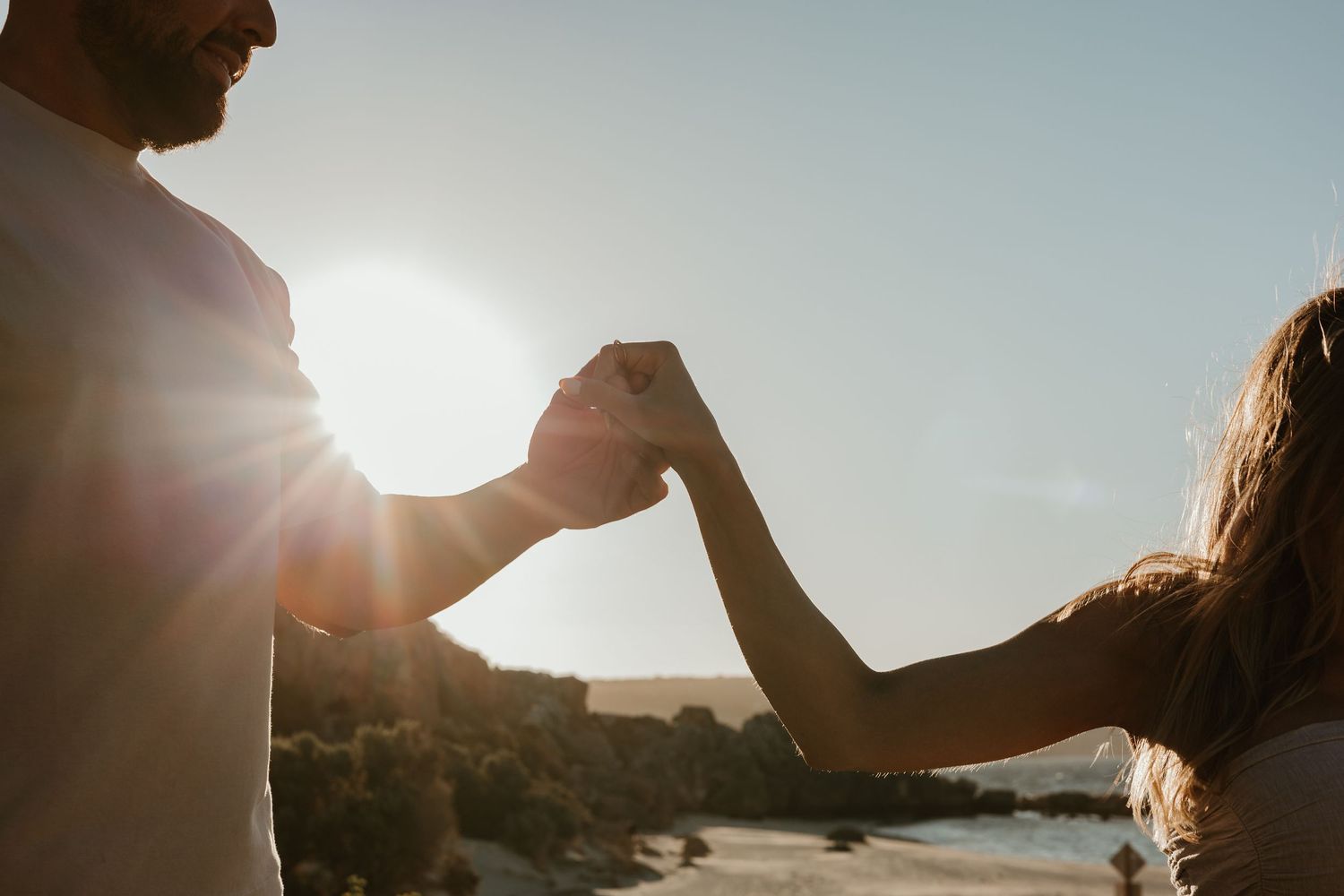 Silhouetted couple holding hands at sunset against natural backdrop.