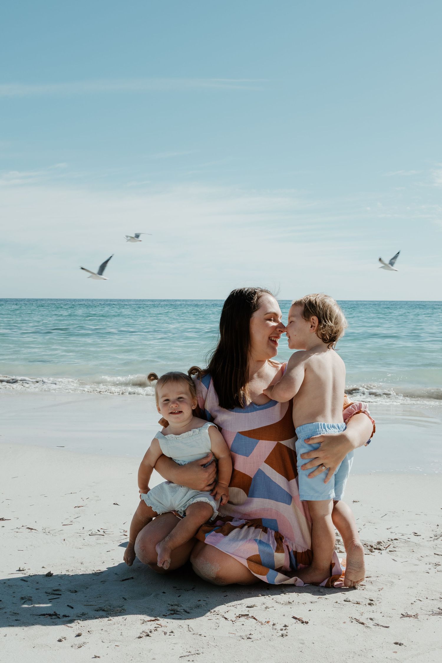 Joyful beach scene with parent and children laughing together as seagulls fly overhead.
