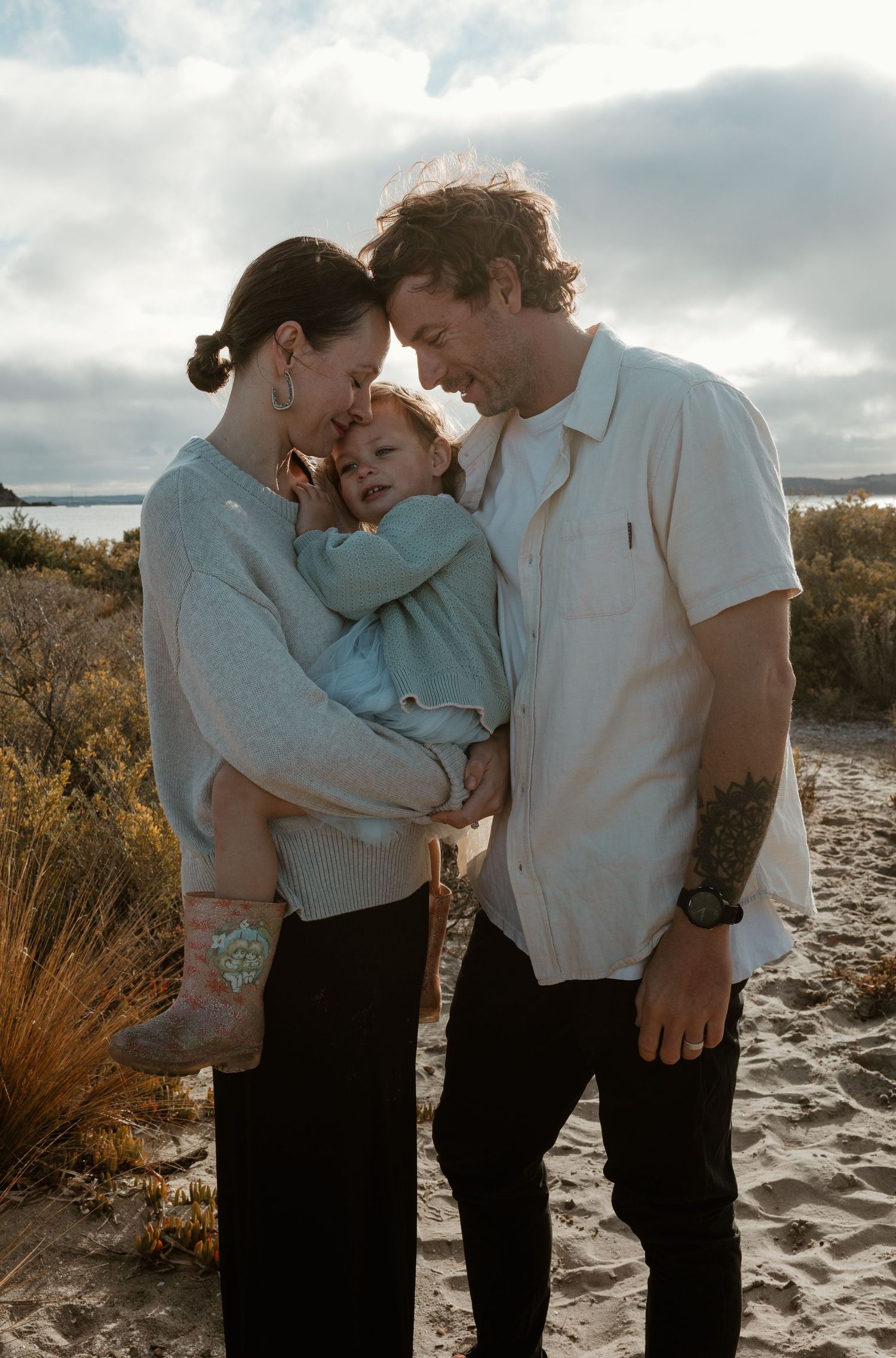 Intimate family moment captured on a cloudy beach with gentle lighting.