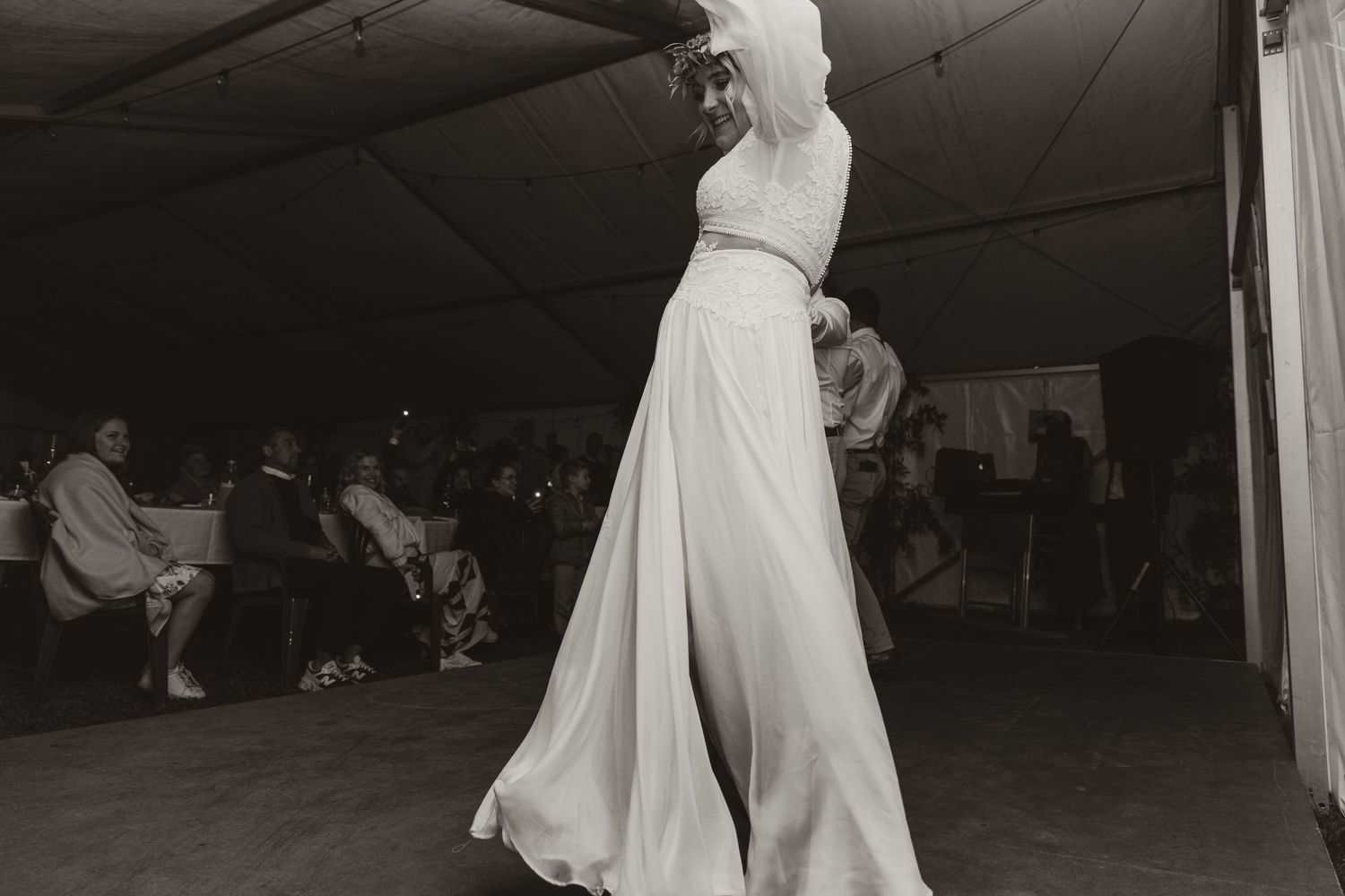 A bride in a flowing white gown dances during her wedding reception in a tent.