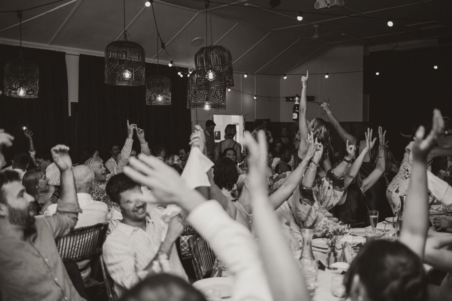 Wedding reception guests raise their hands in celebration during a lively dance party moment.