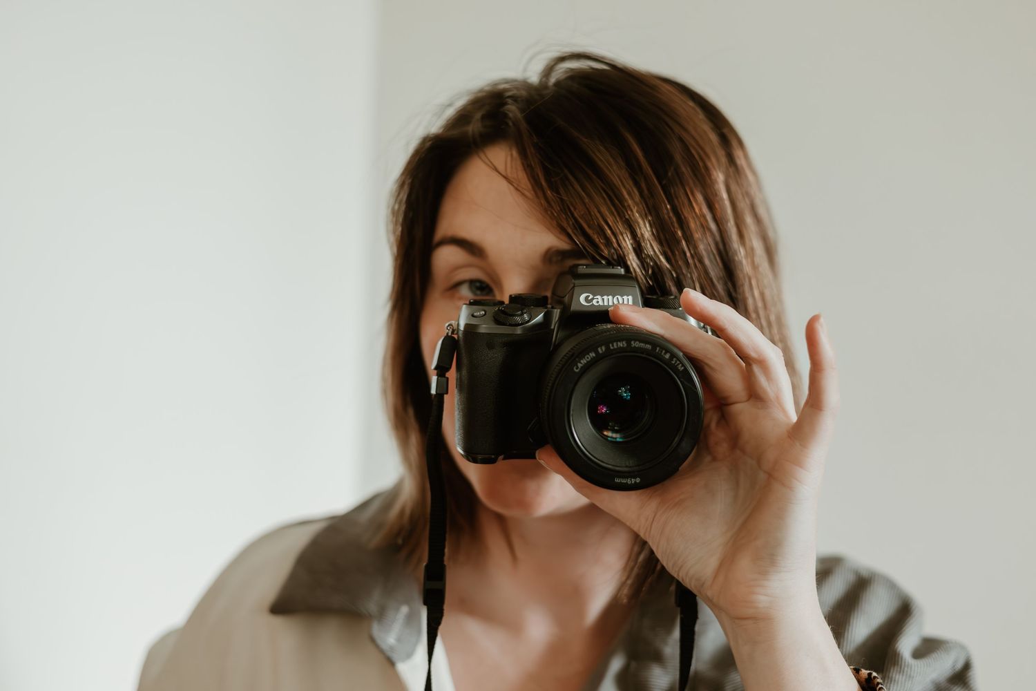 Person holding professional camera up to take photo against white wall.
