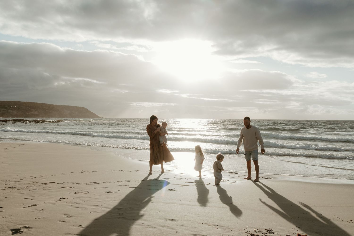 Family silhouettes walking on Kangaroo Island beach at sunset casting long shadows.