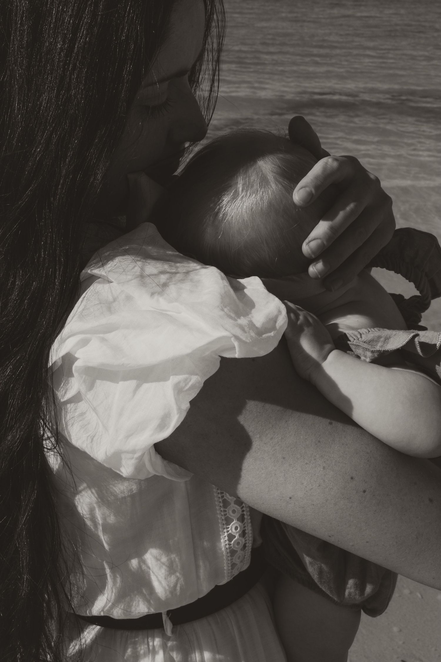 Intimate black and white portrait of mother cradling baby in white dress. Kangaroo Island.