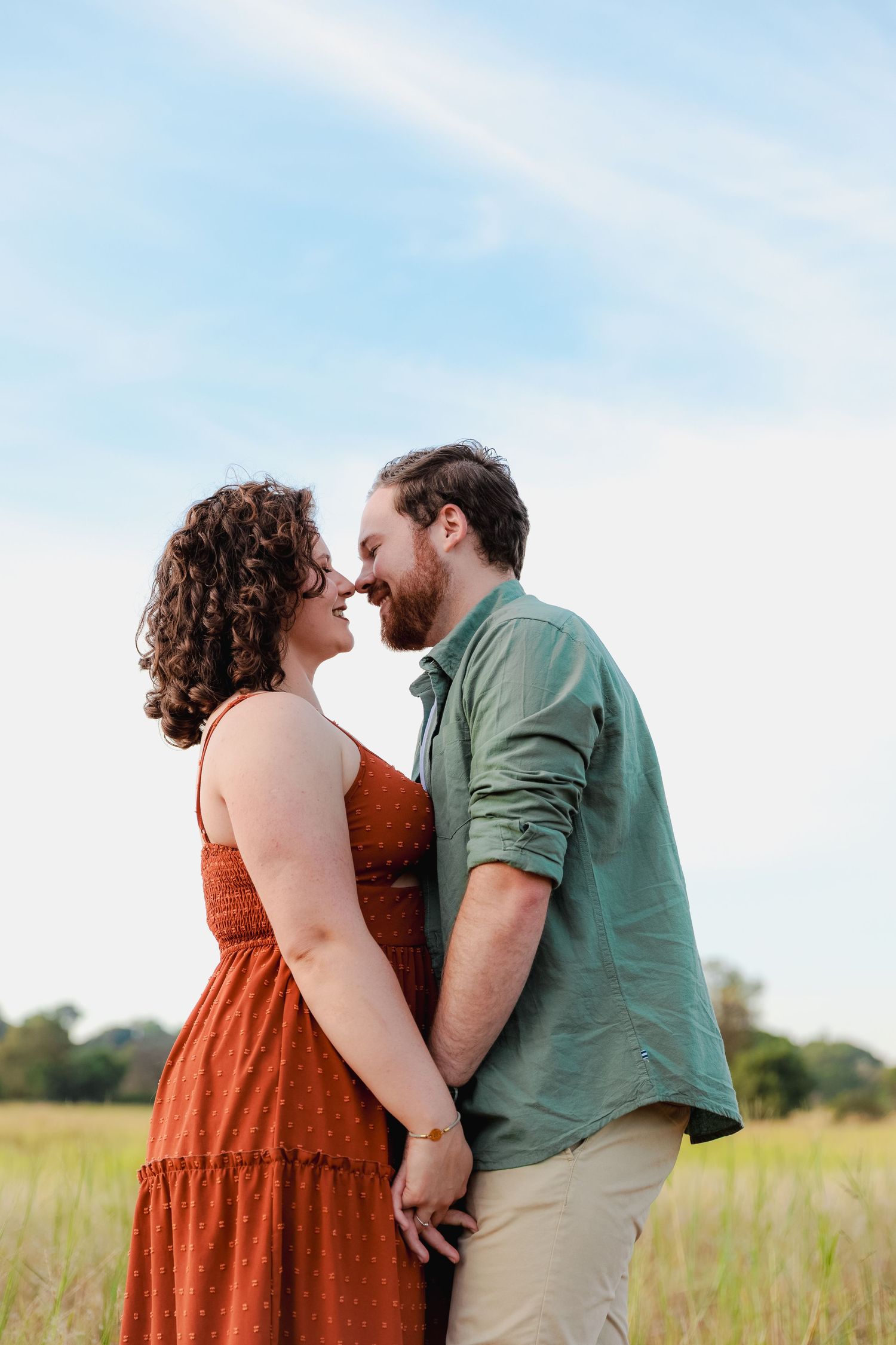 A romantic couple shares an intimate moment while standing in a golden field under a soft blue sky.