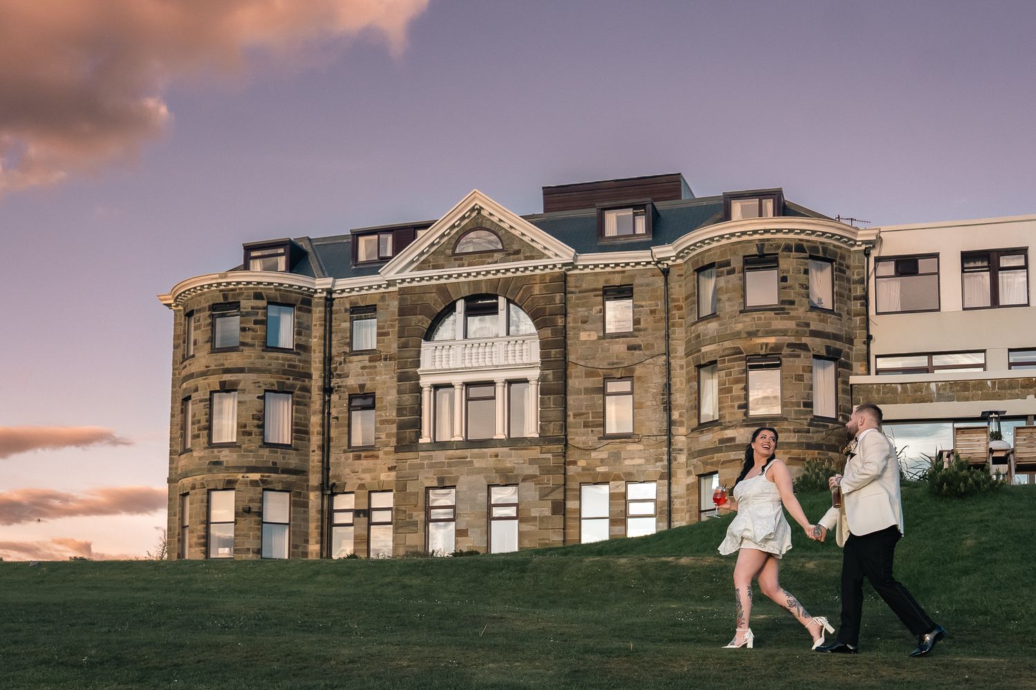 Bride and groom walking across the grounds at sunset outside Grand Villa Heights.