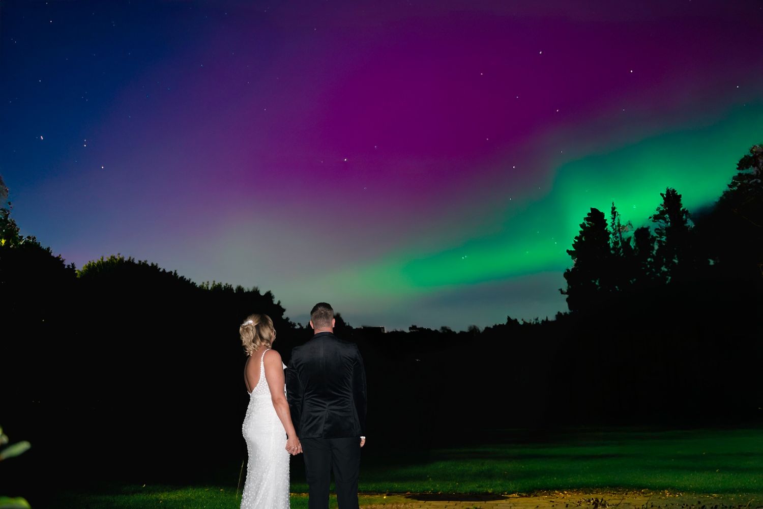 Bride and groom standing outdoors under the northern lights in the gardens at Lazaat Hotel, Hull.