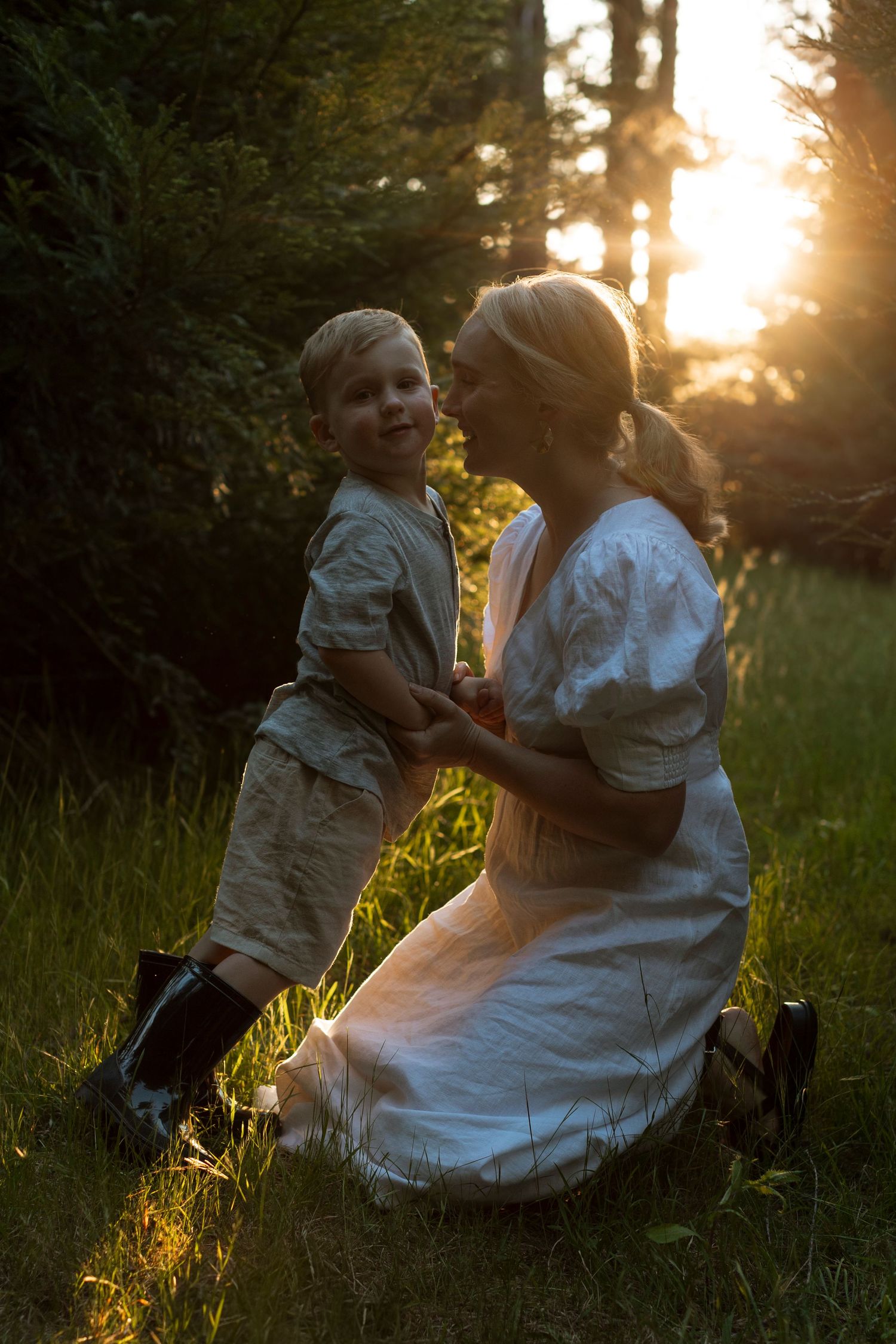 Mother and child sharing playful moments in sunlit meadow at sunset.