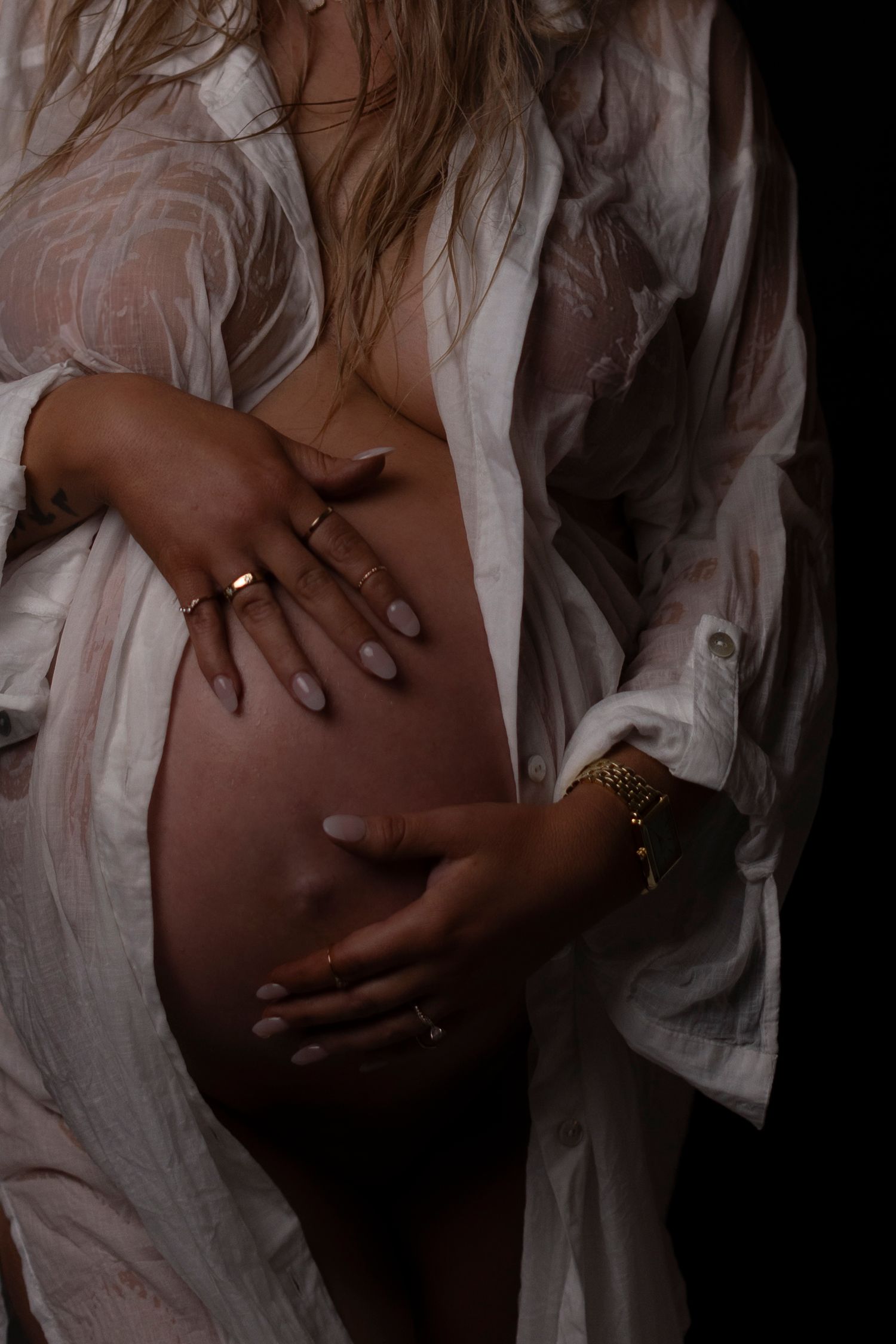 Close-up of hands cradling pregnant belly through sheer white fabric.