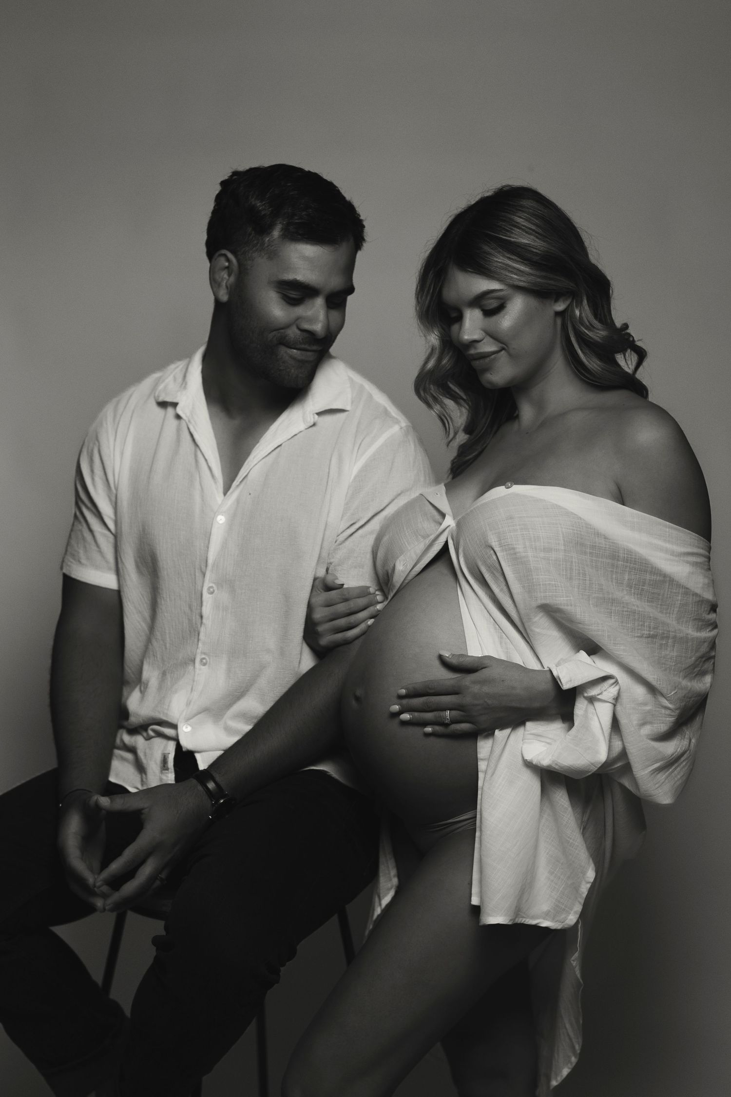 Black and white maternity photo of couple in white shirts embracing.