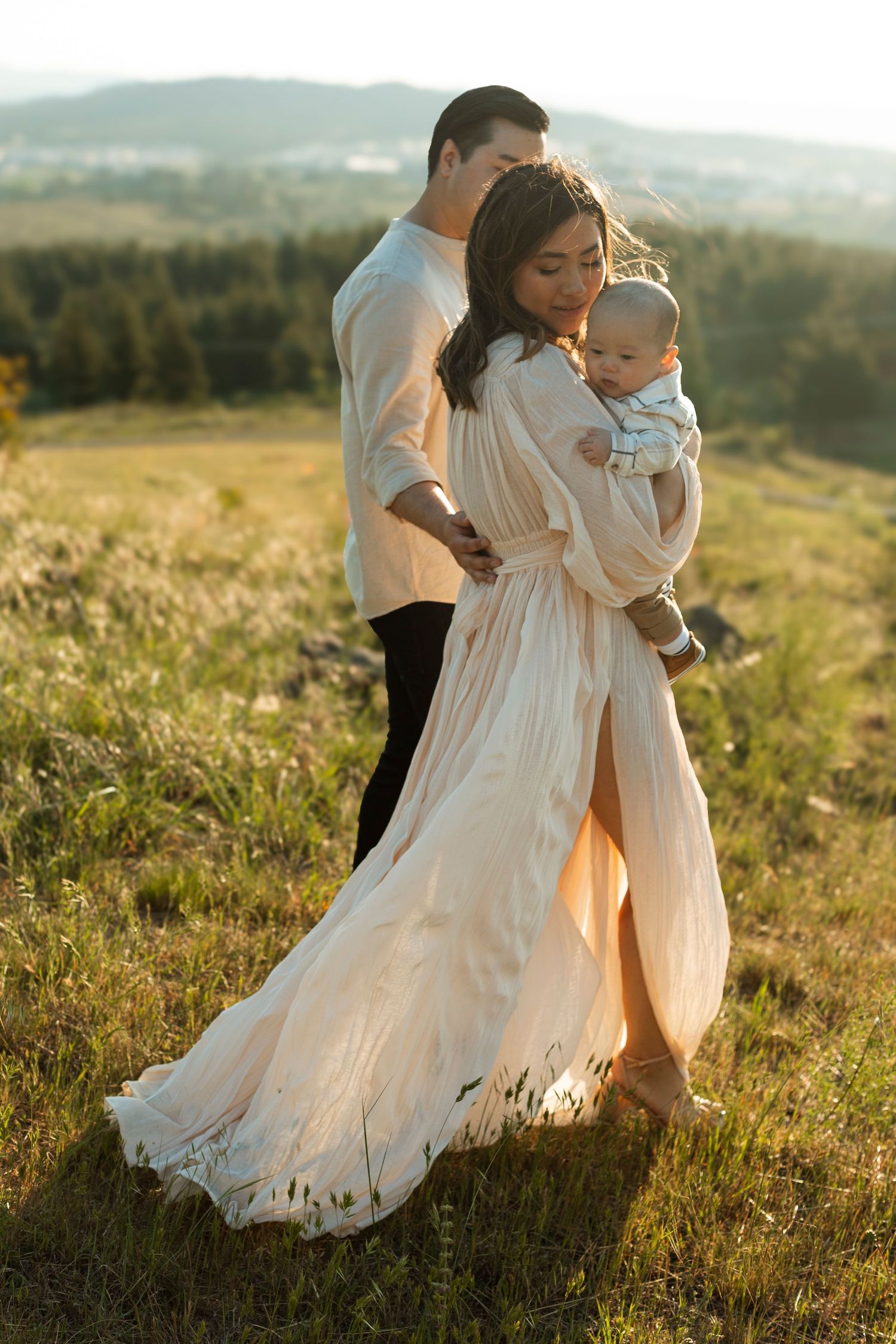 Family in white clothing dancing together in sunlit meadow with mountains in background.