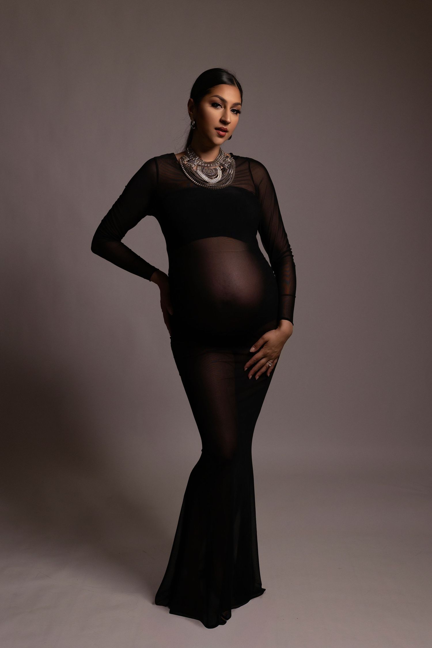 Fashion model poses in a flowing black dress against a neutral studio backdrop in a series of elegant poses.
