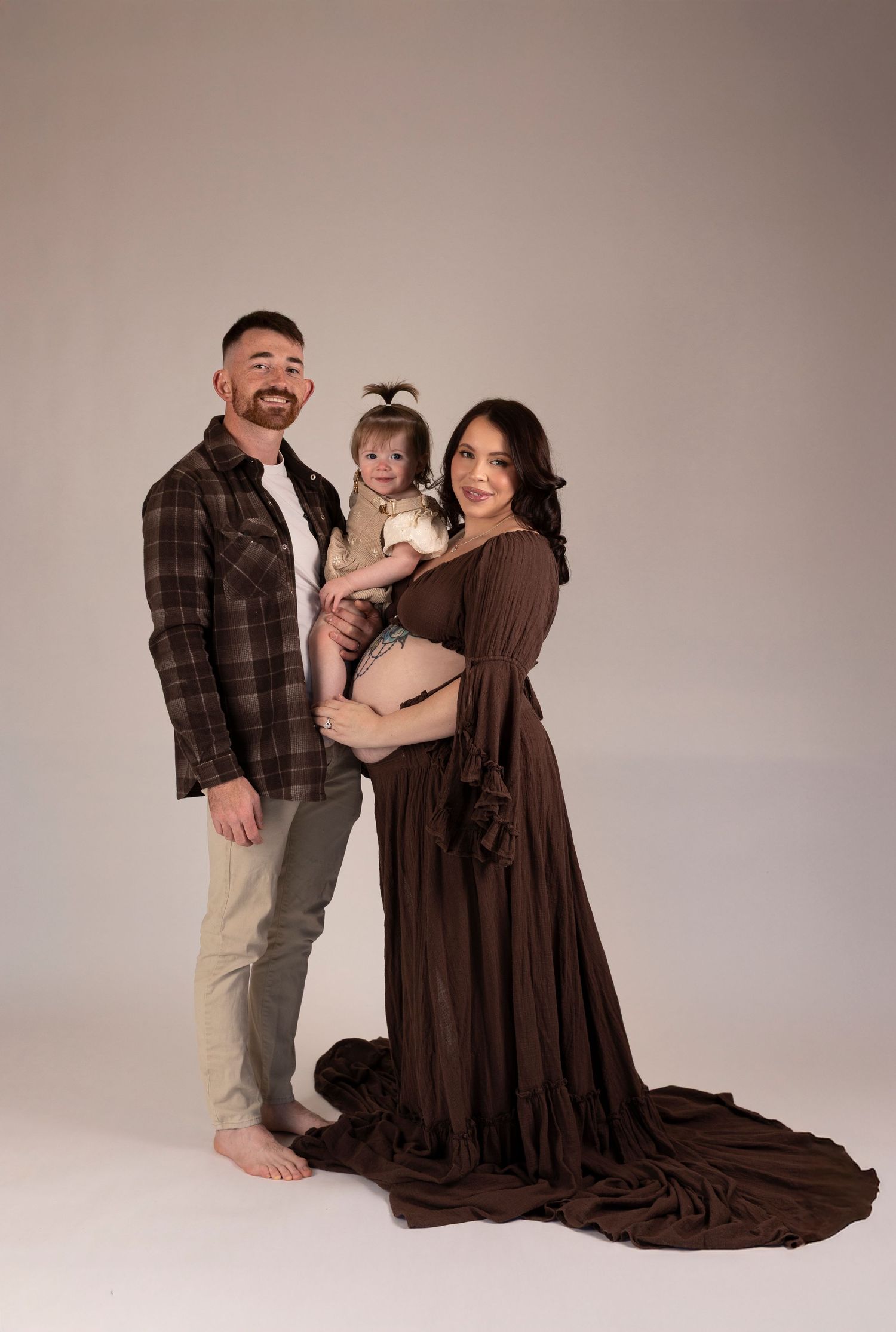 Family portrait featuring parents and child in coordinating brown tones with flowing dress.