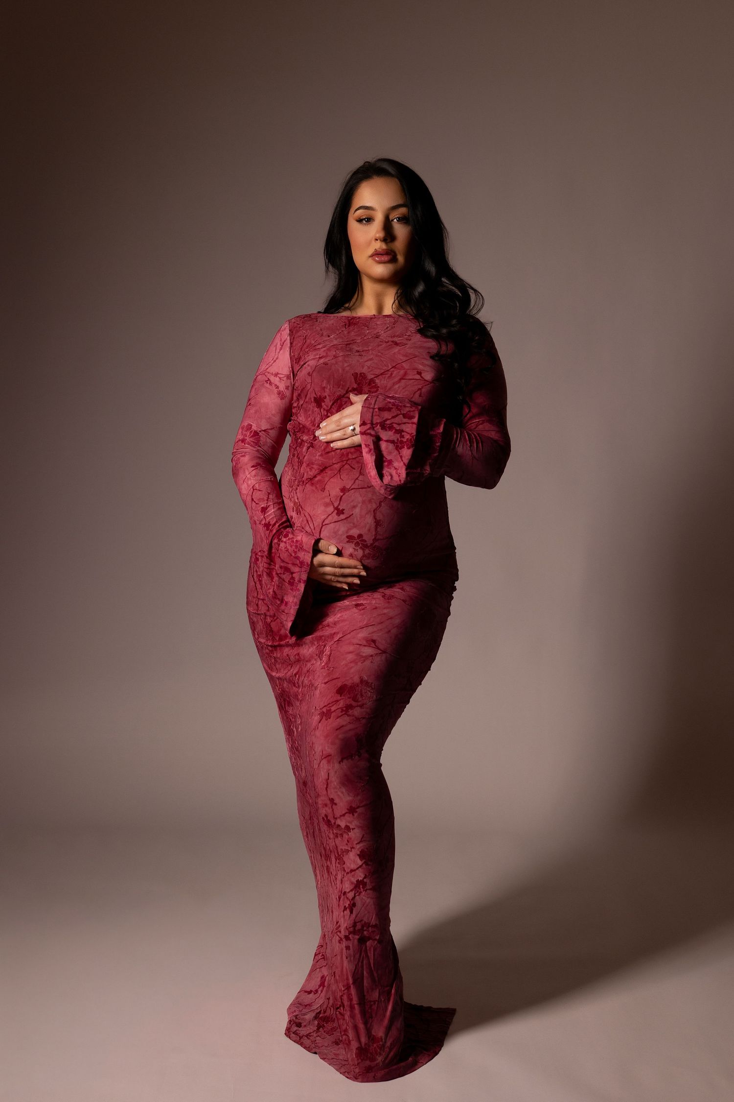 A model poses in a burgundy textured velvet gown against a neutral studio backdrop in a fashion photography series.