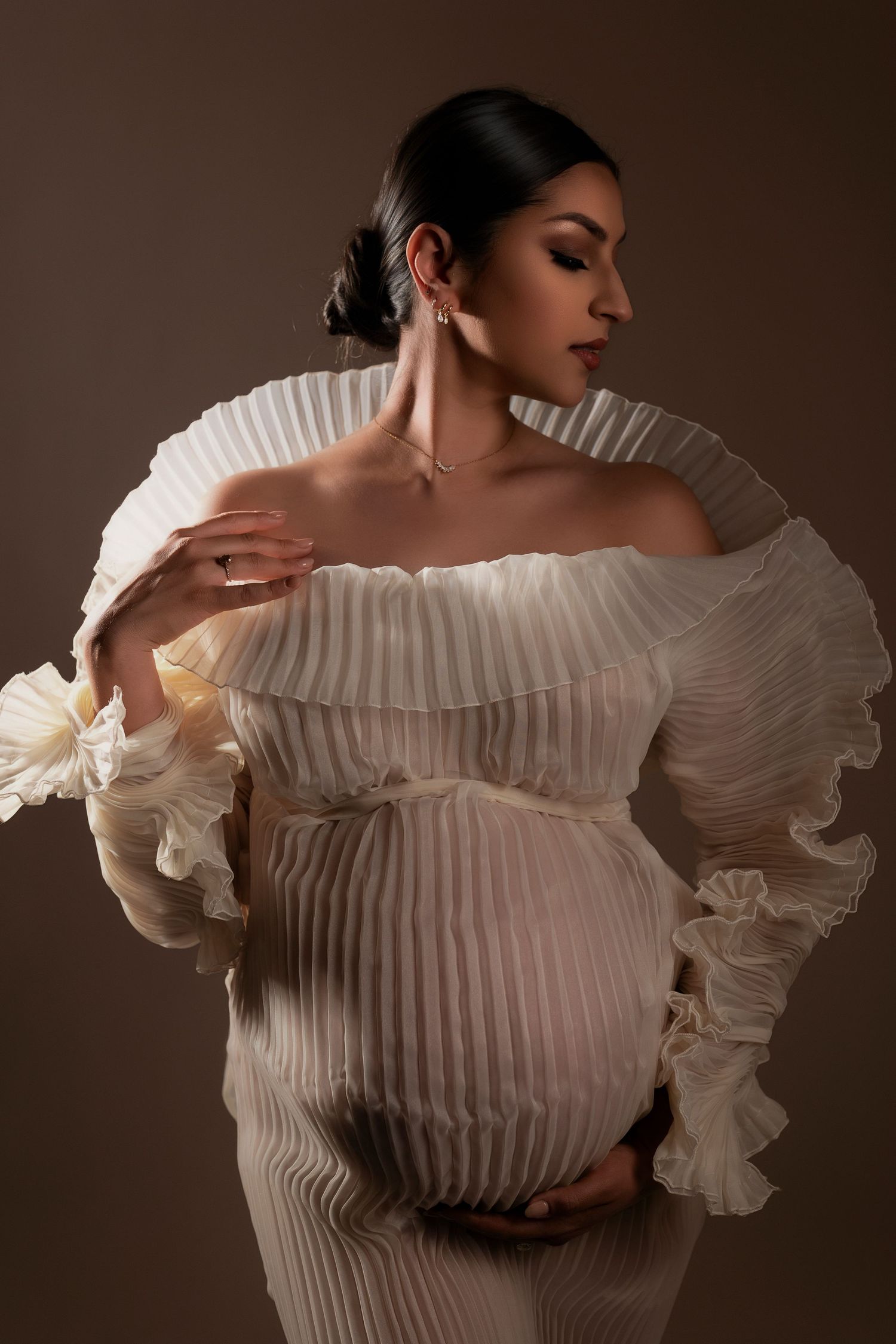 Fashion model wearing dramatic white pleated off-shoulder top with ruffled sleeves in elegant studio portrait series.