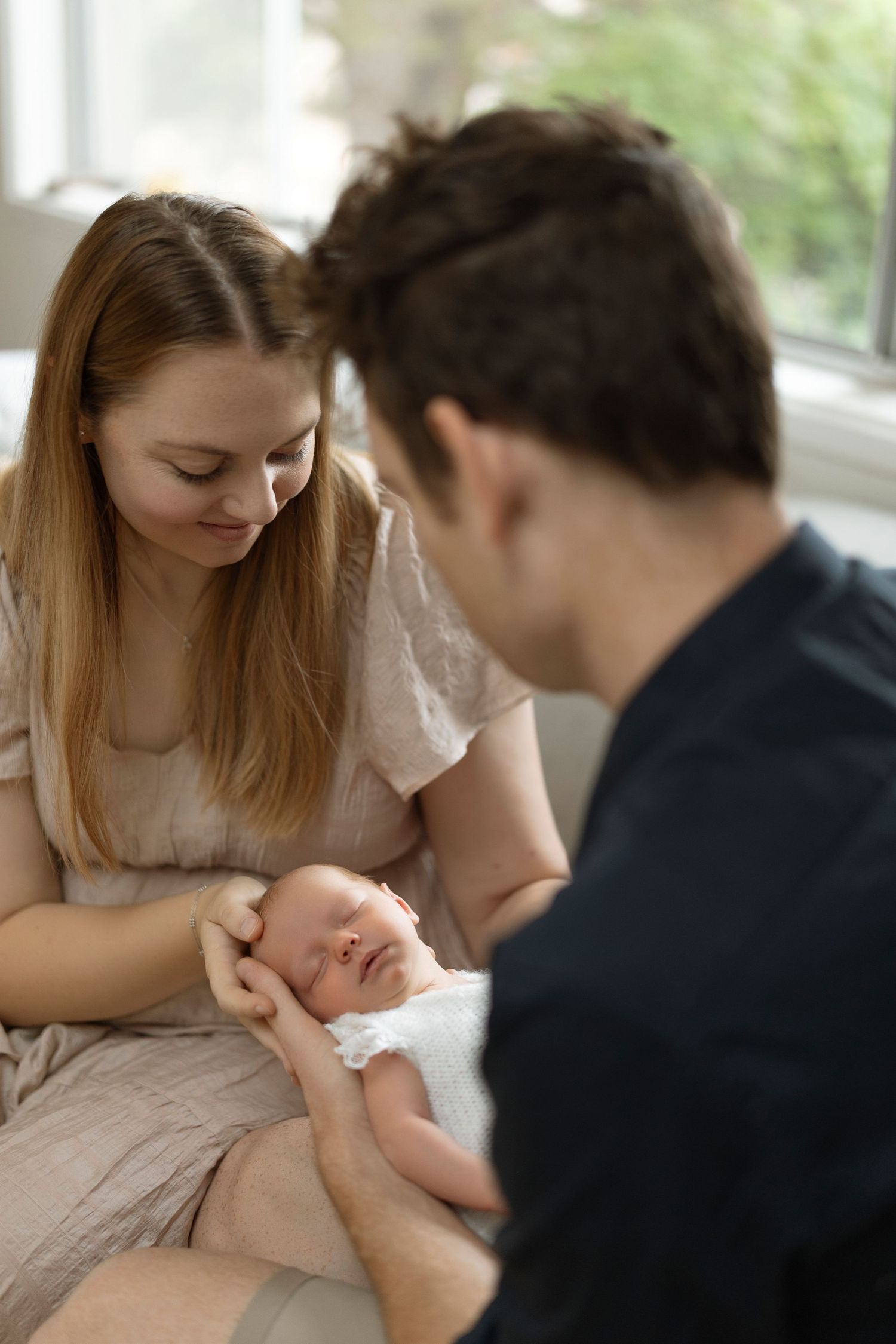 Parents gazing lovingly at their newborn baby during an indoor lifestyle photoshoot.