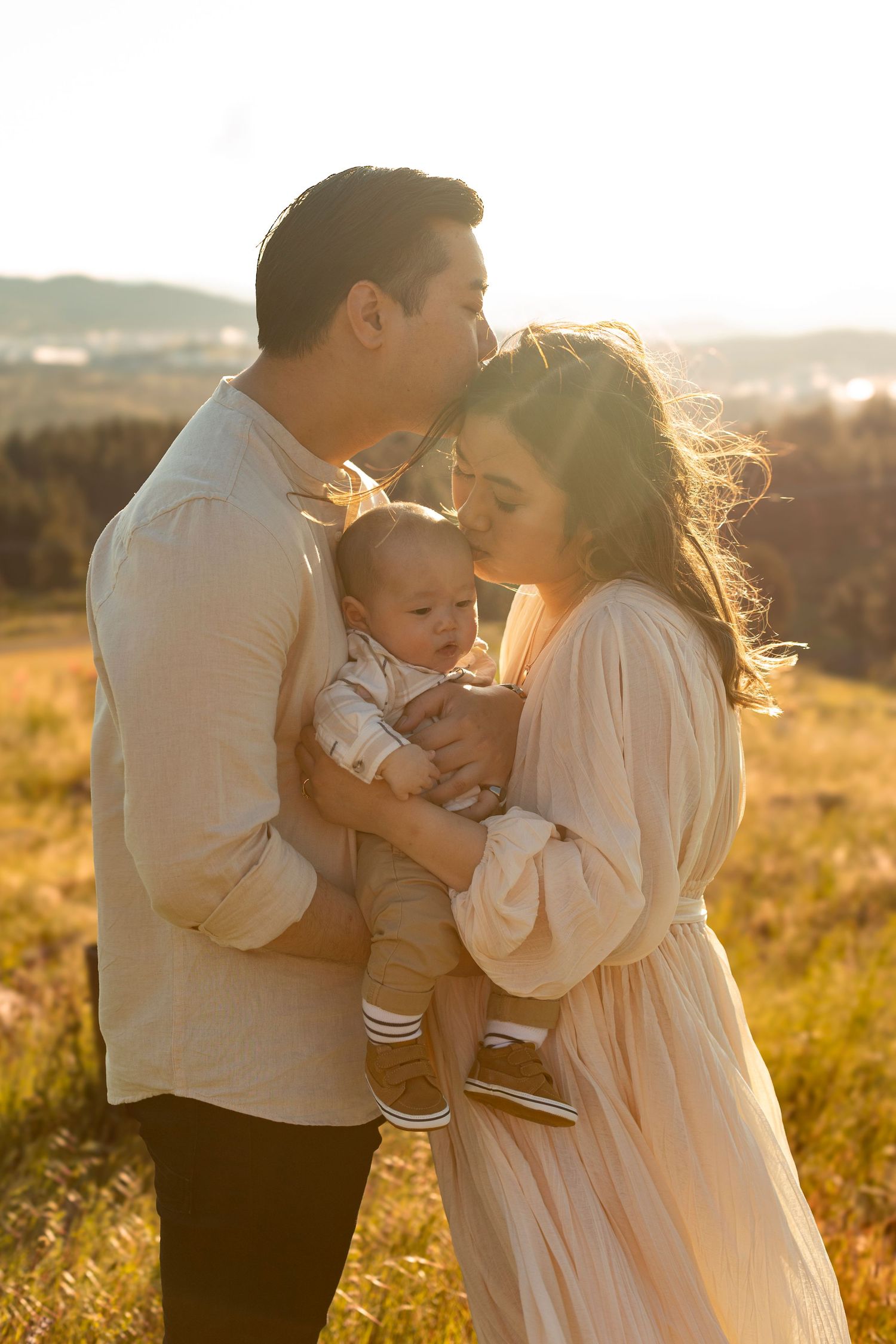 Family sharing intimate embraces in golden sunlit field during sunset photoshoot.