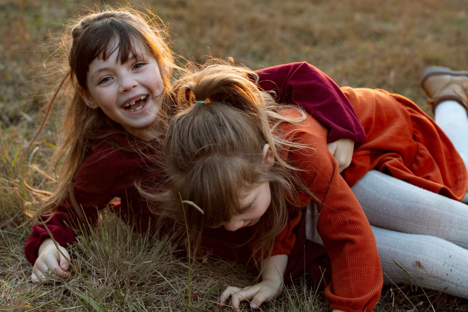 Child in red dress playing and laughing in golden grass field.