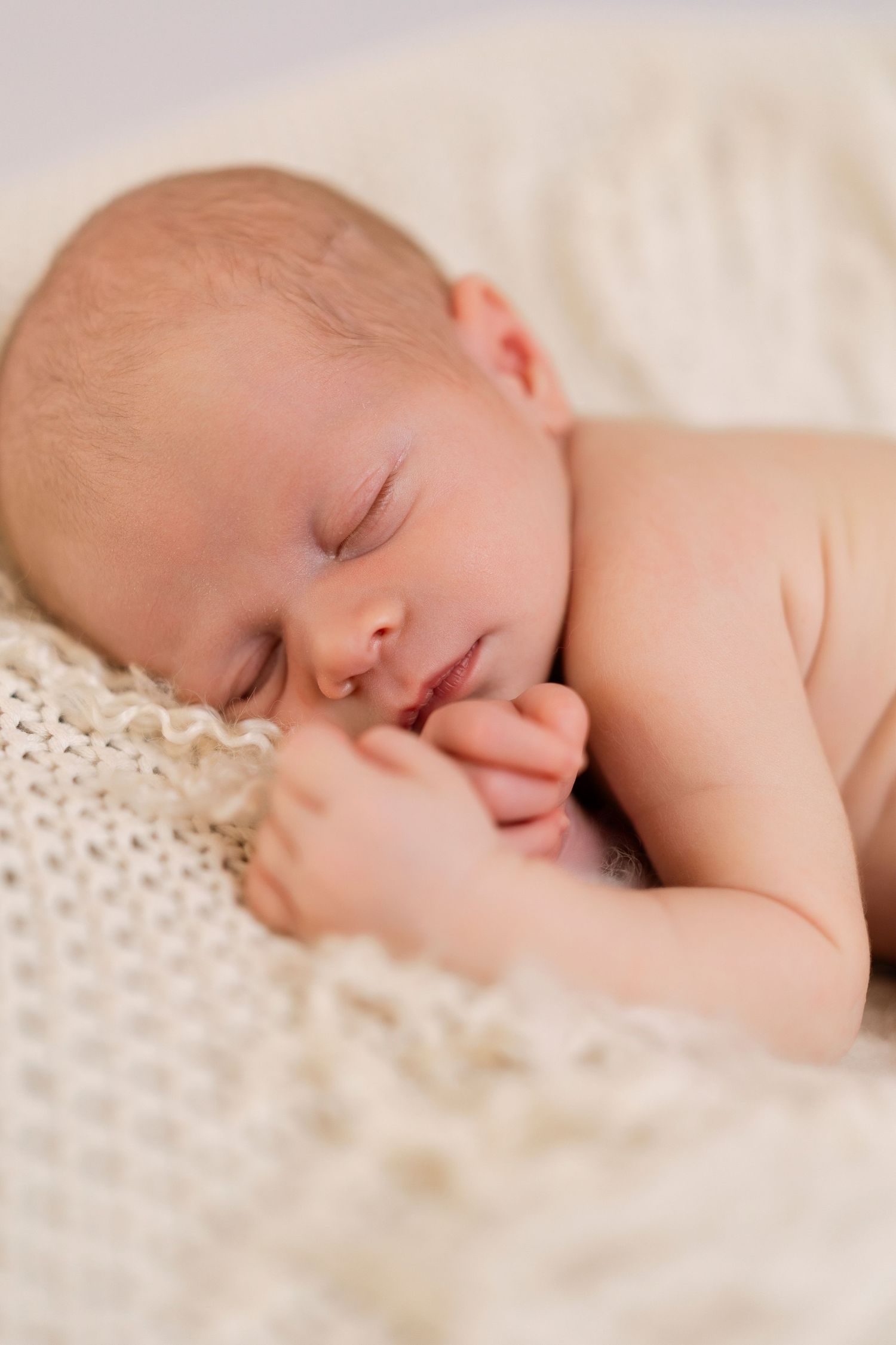 Peaceful sleeping newborn baby rests on soft white knit blanket during professional photo session.