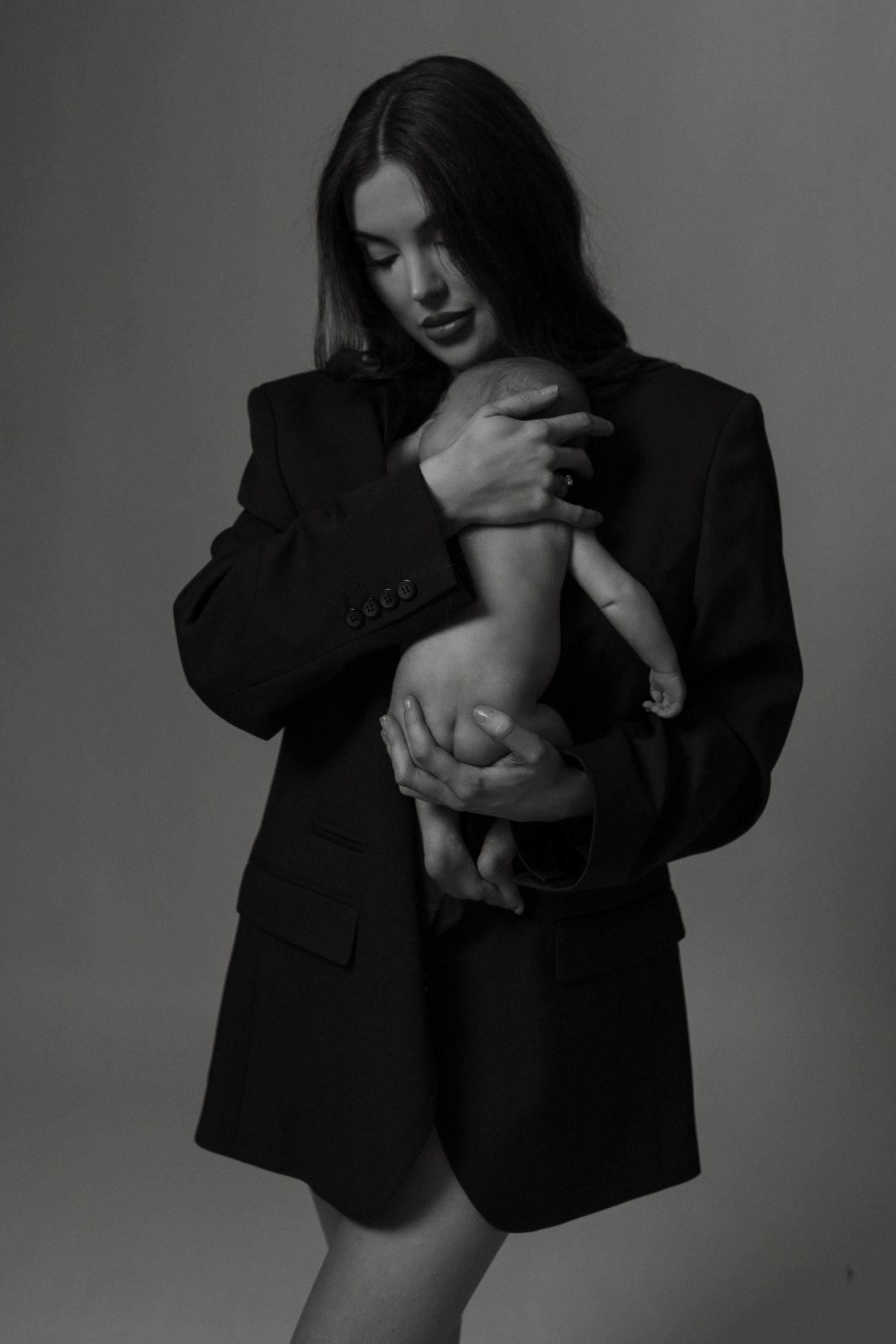 A person in a dark blazer holds and cradles a small pet against their chest in a series of black and white photos.