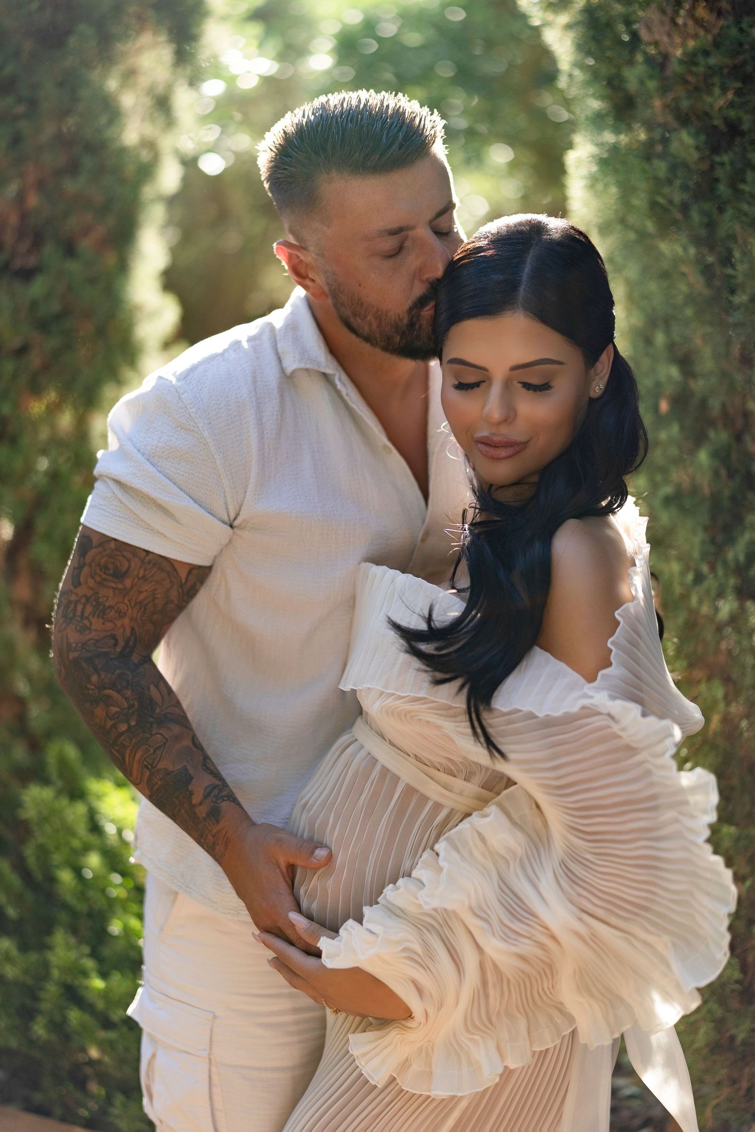 A romantic couple in white outfits embrace in a dreamy garden setting with soft bokeh lighting effects.
