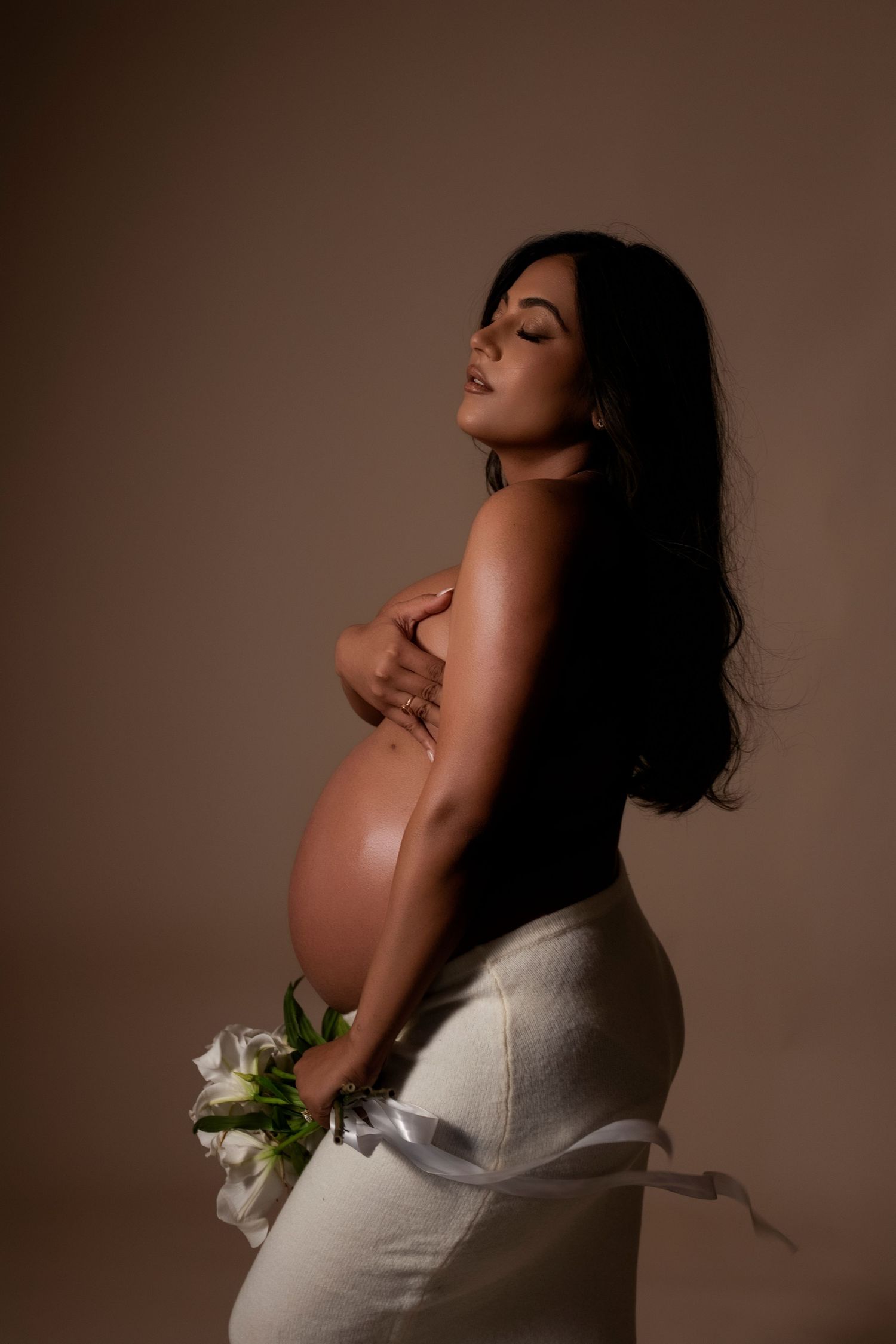 Artistic maternity photo series showing a pregnant woman in white against brown backdrop in various graceful poses.