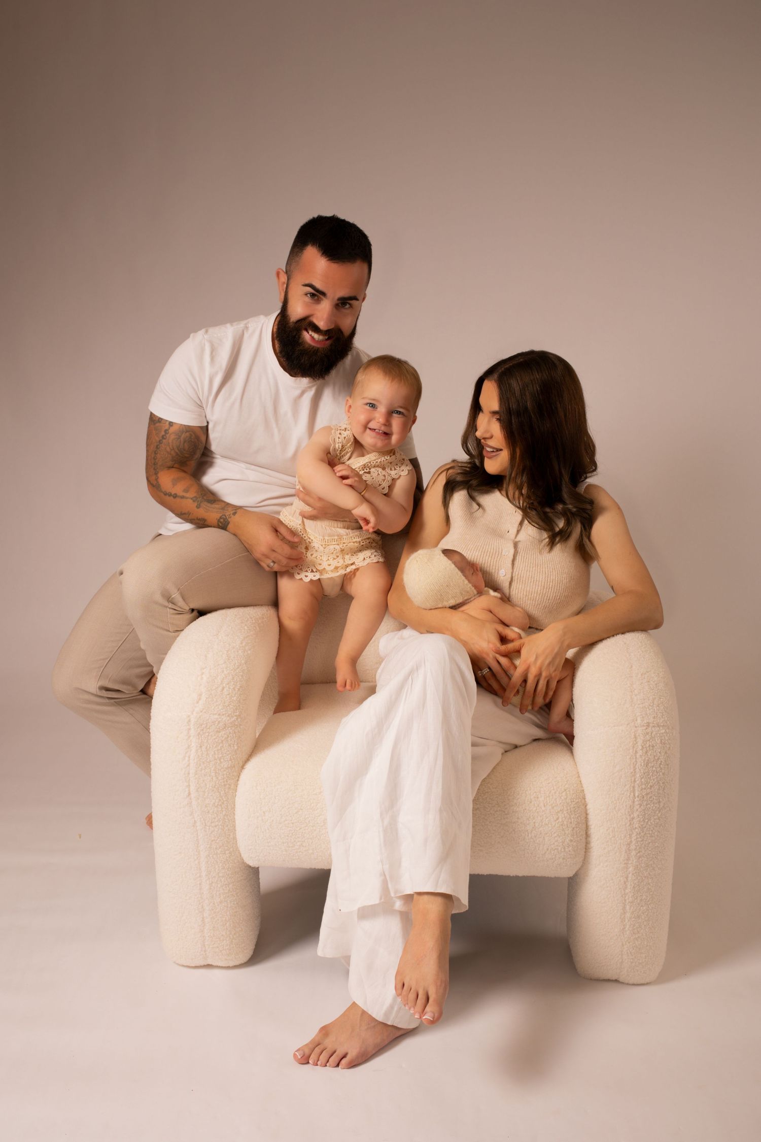 Family portrait on cream couch featuring casual styling in neutral tones.