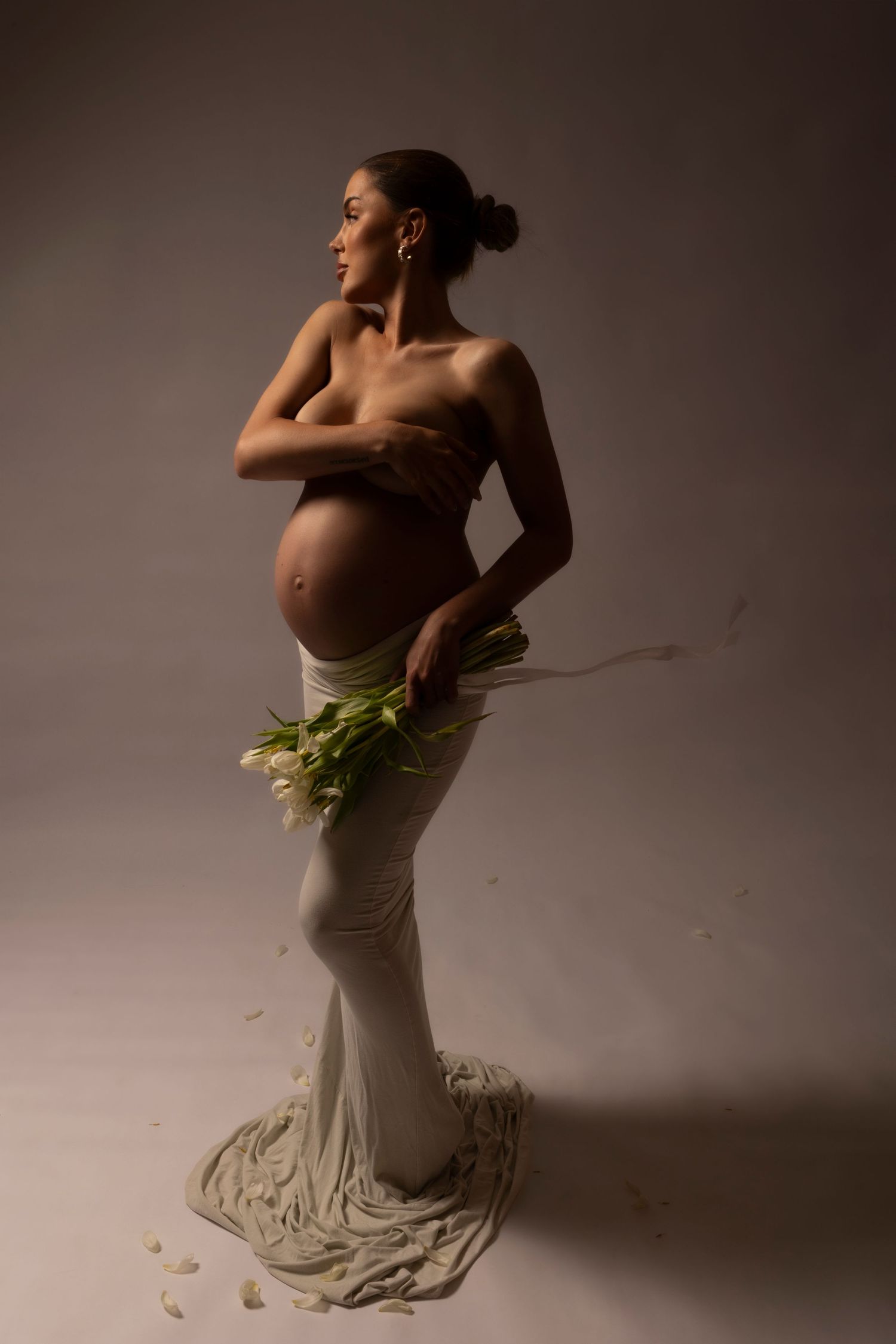 Dramatic maternity portrait with flowing fabric and fresh flowers in studio setting.