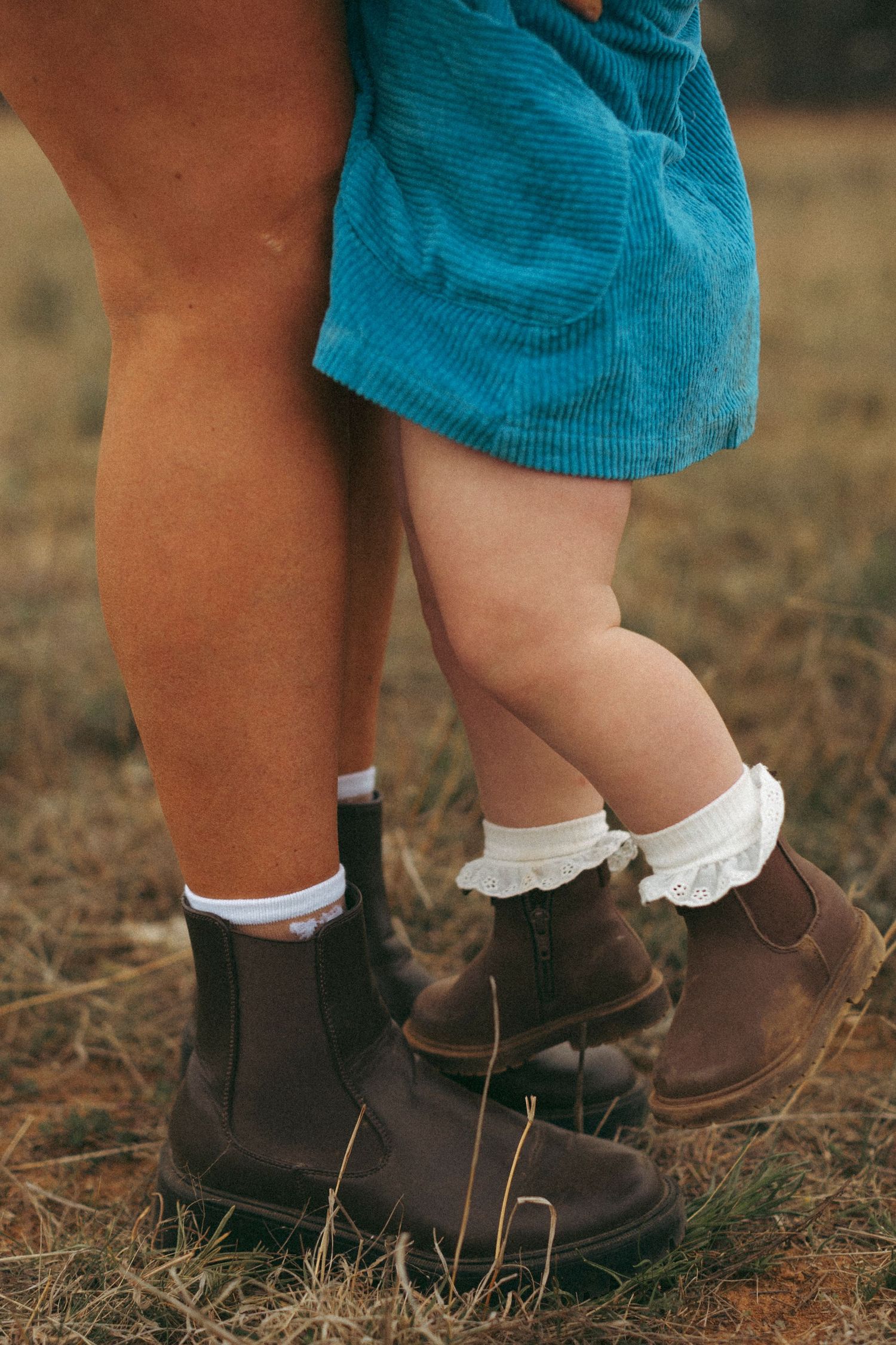Close-up of tiny feet wearing brown boots and white socks on rustic ground.
