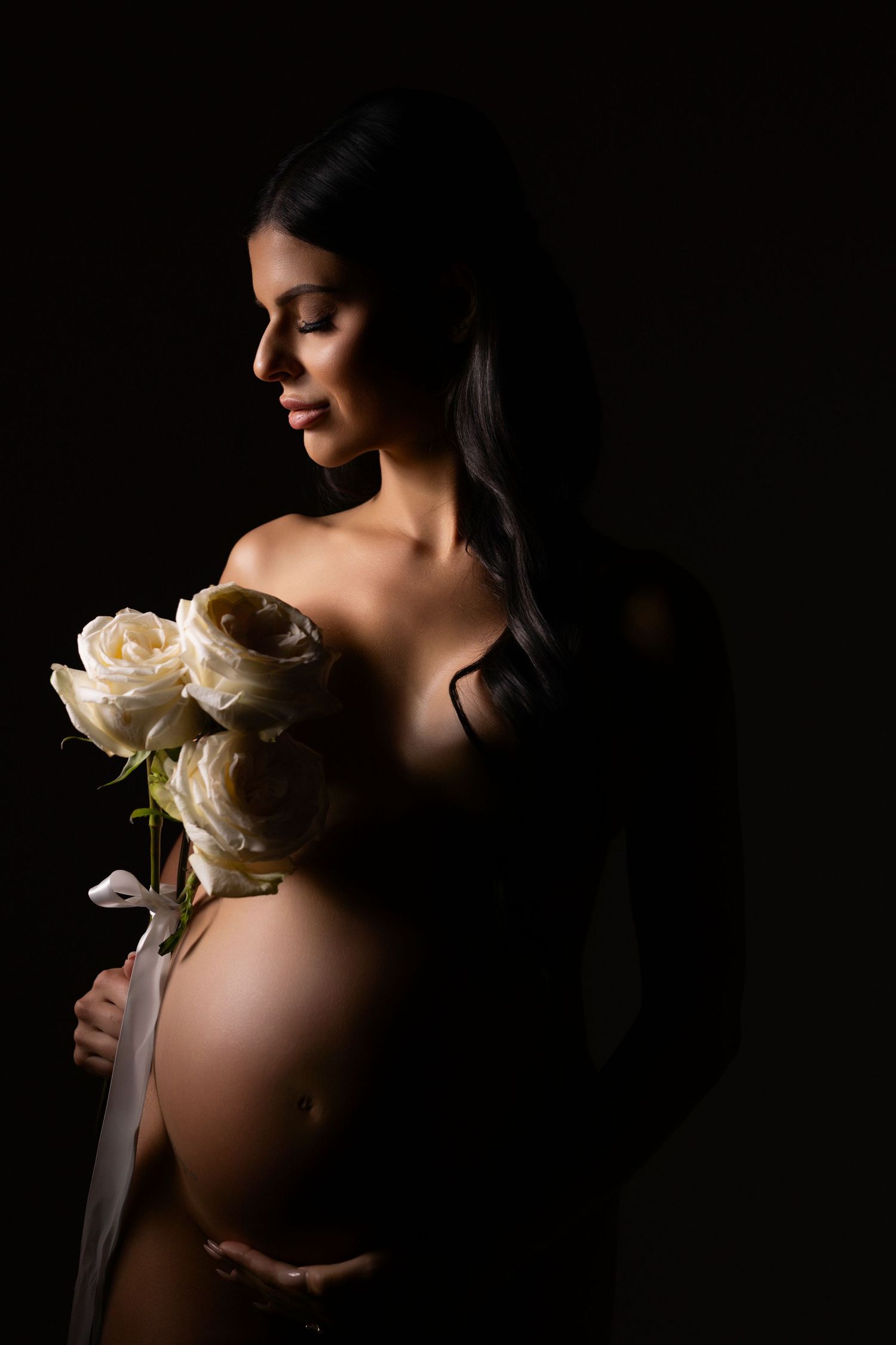 Artistic maternity silhouette series showing pregnant figure with white flowers against dark background.