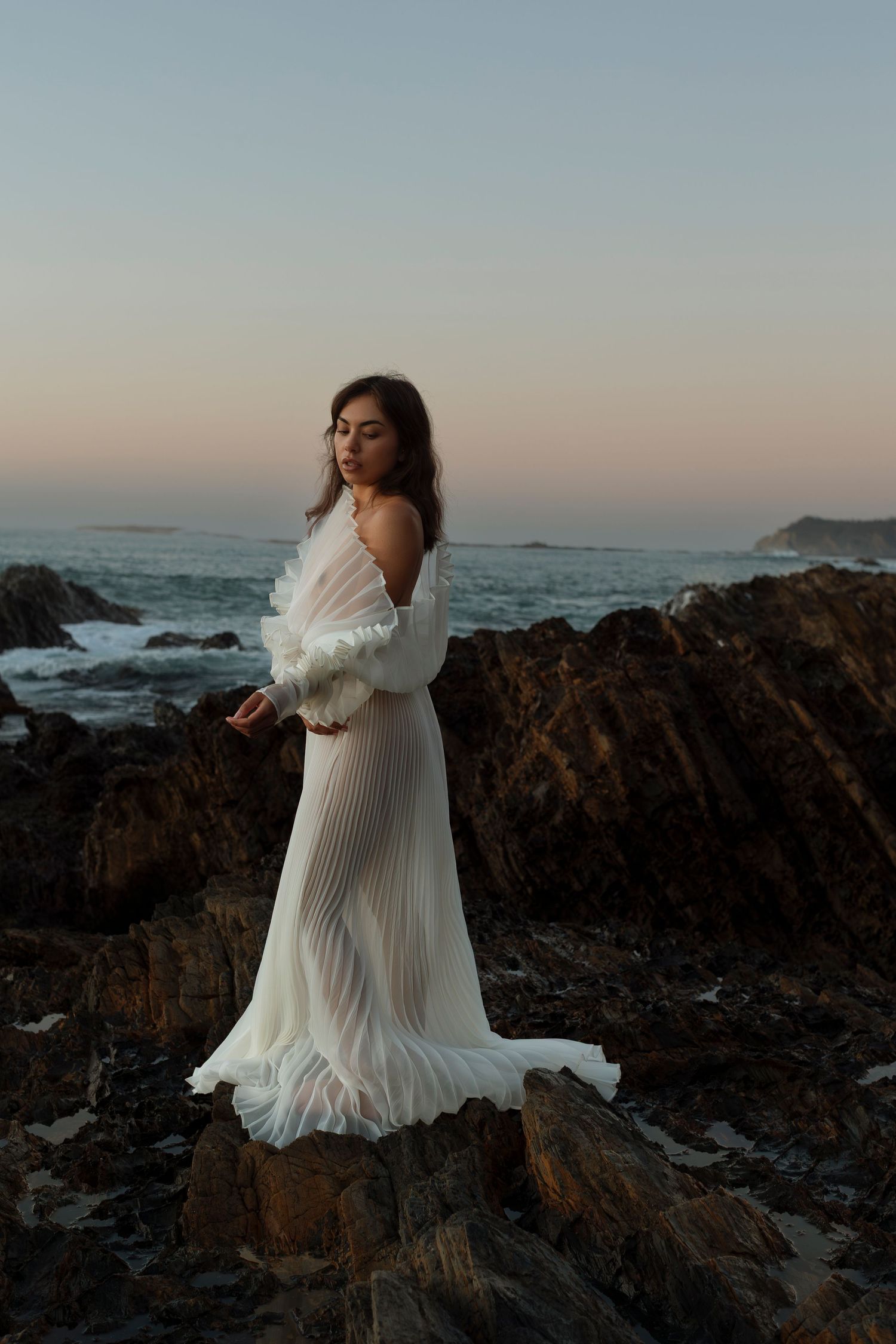 Elegant white dress movement captured against dramatic rocky coastline.