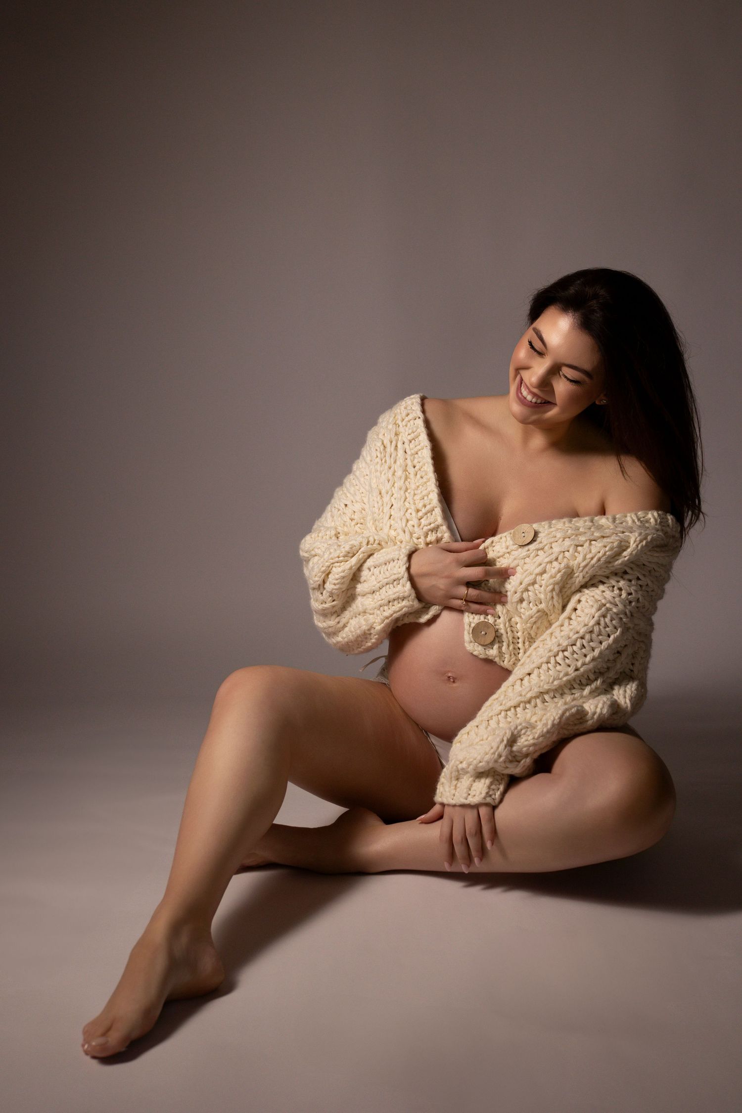 Artistic maternity photo series showing a pregnant belly in cream sweater against neutral background.