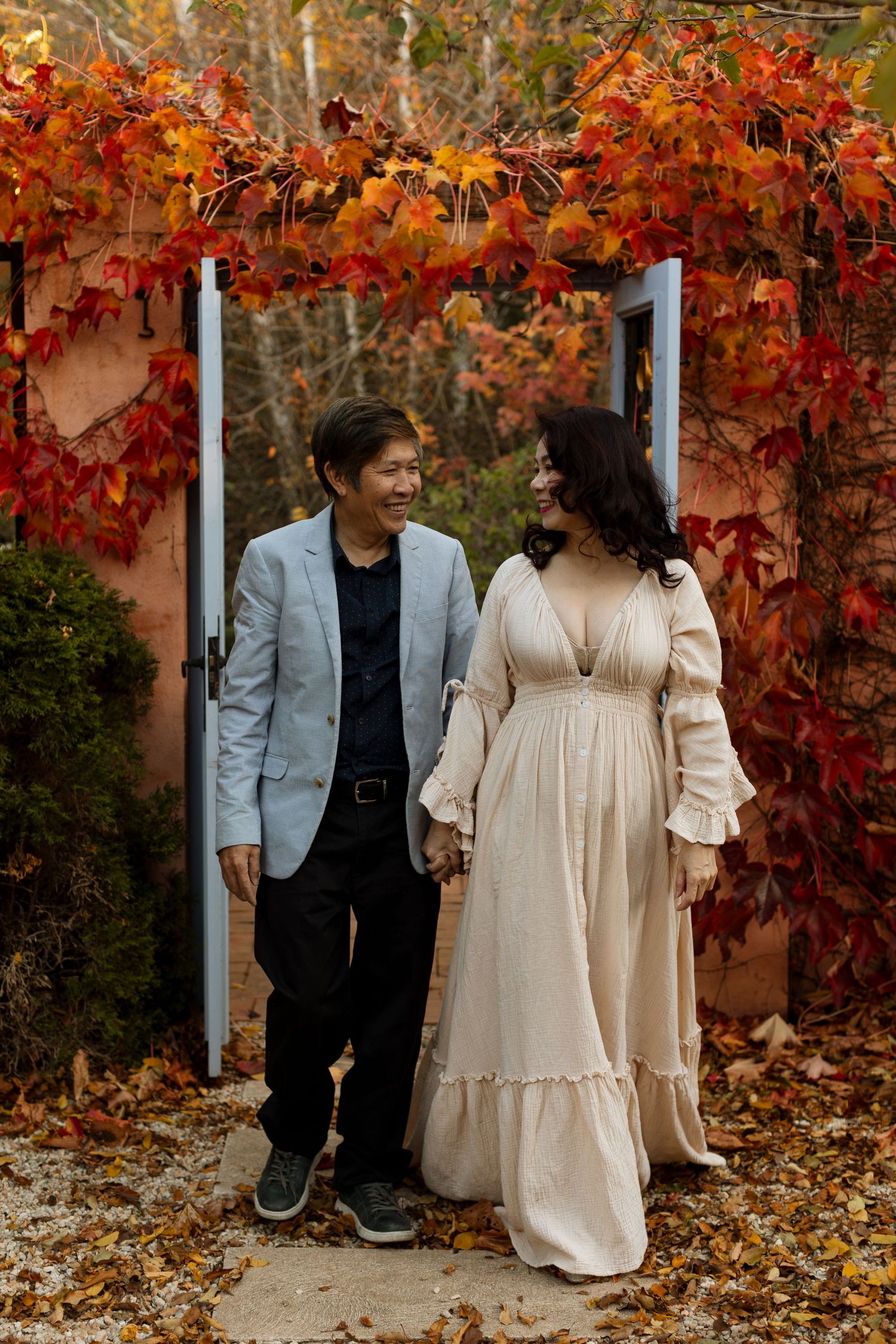 A couple sits together on a bench surrounded by vibrant autumn foliage with red and orange leaves.