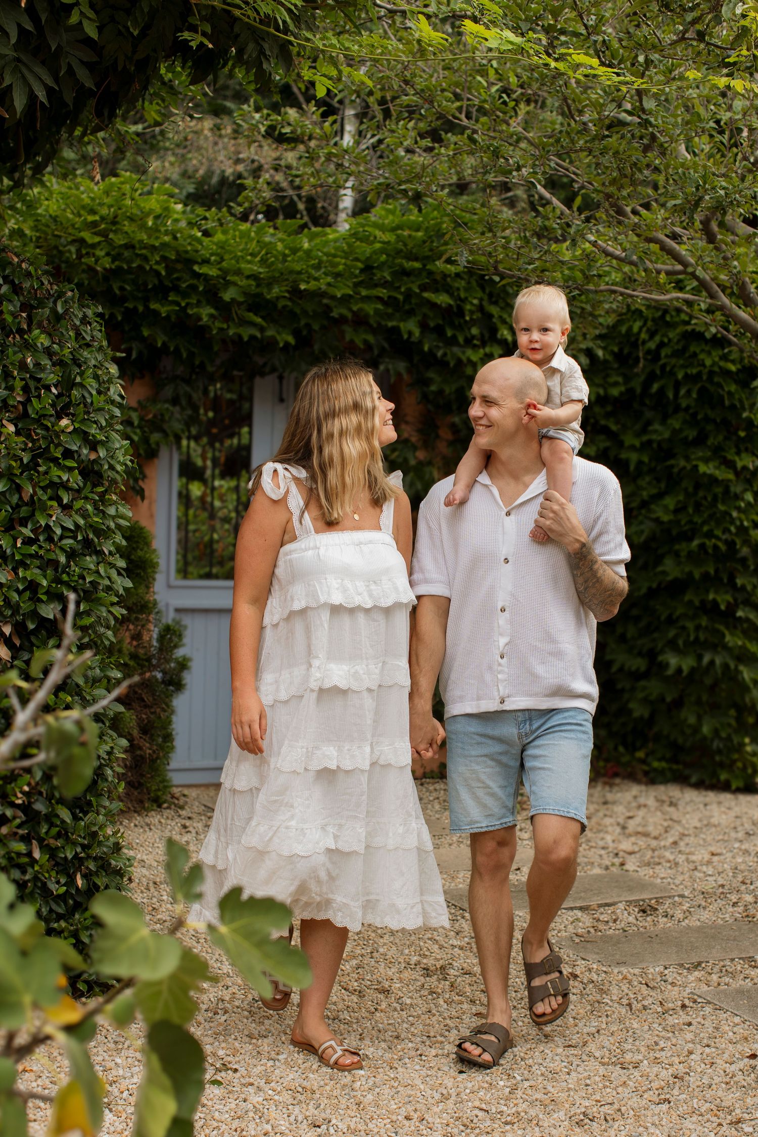 Family walking together on a gravel path through a lush garden wearing coordinated white outfits.