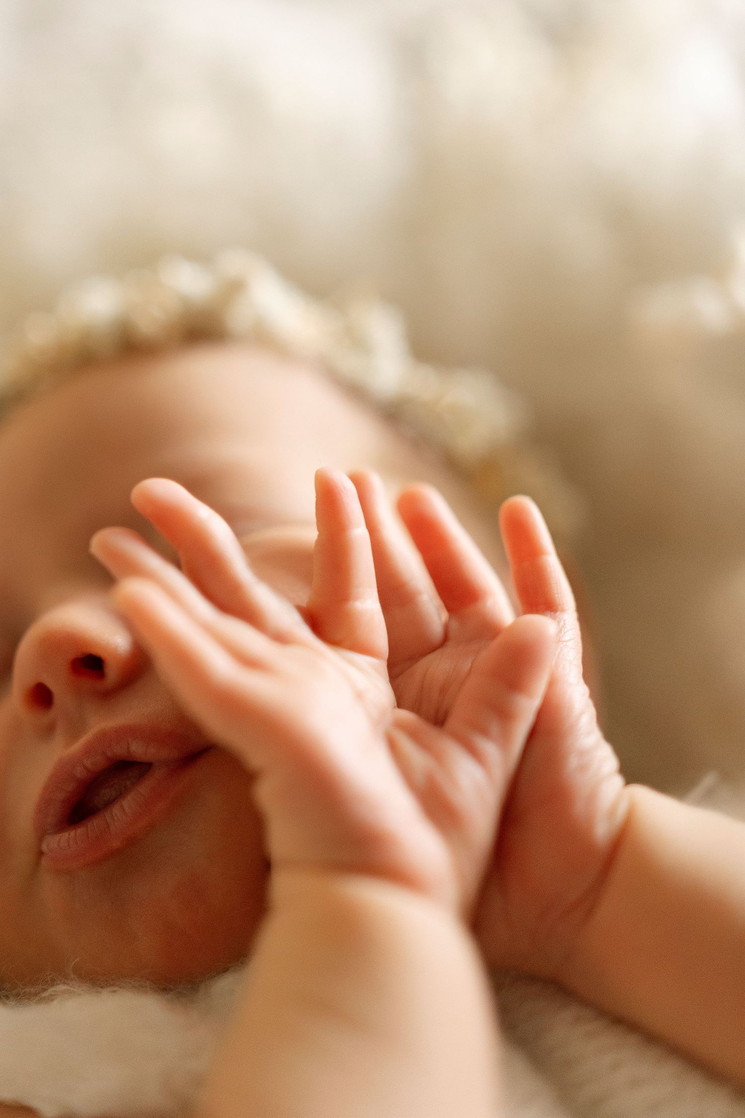 Close-up of tiny newborn baby hands reaching upward against a soft beige background.