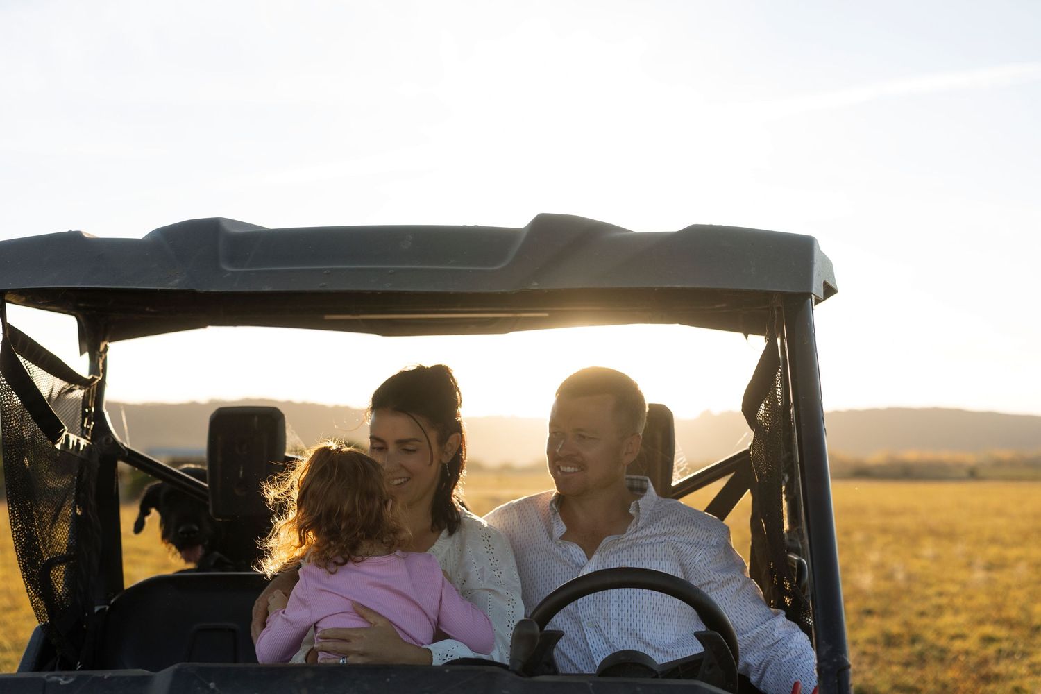 Family enjoying a sunset ride in an off-road utility vehicle across an open field.