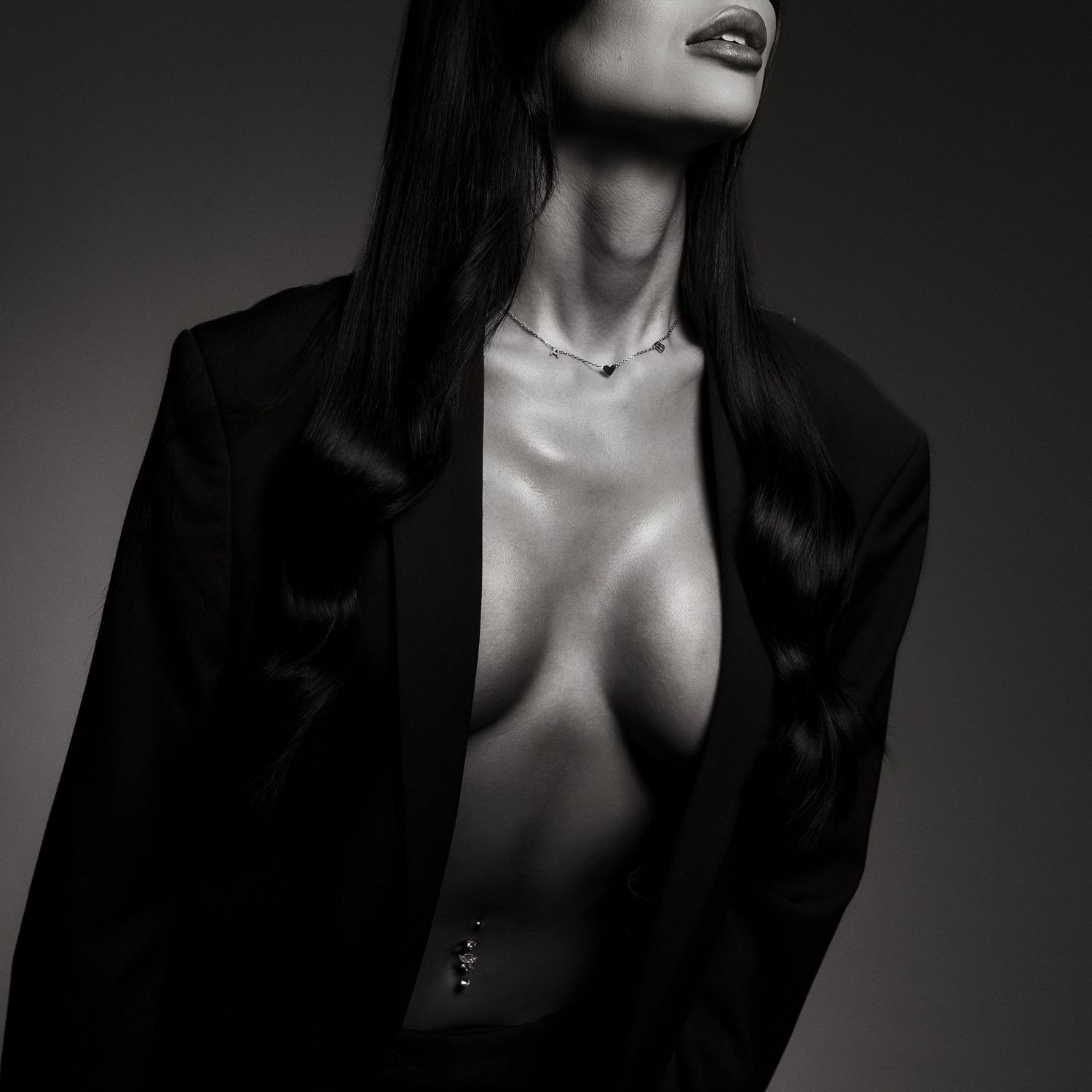Black and white portrait of a woman in an open black blazer with a delicate necklace, dramatic studio lighting.