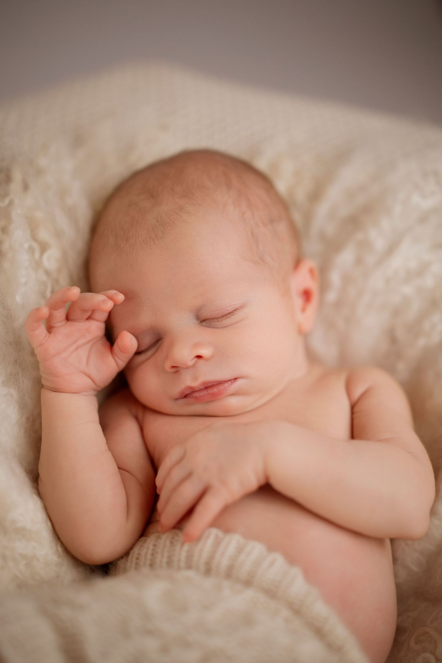 Peaceful sleeping newborn baby curled up on soft cream-colored blanket in natural light.