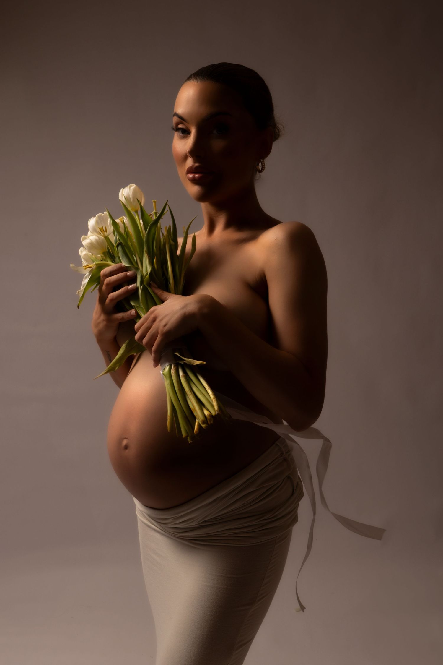 Elegant maternity portrait featuring white calla lilies against dark backdrop.