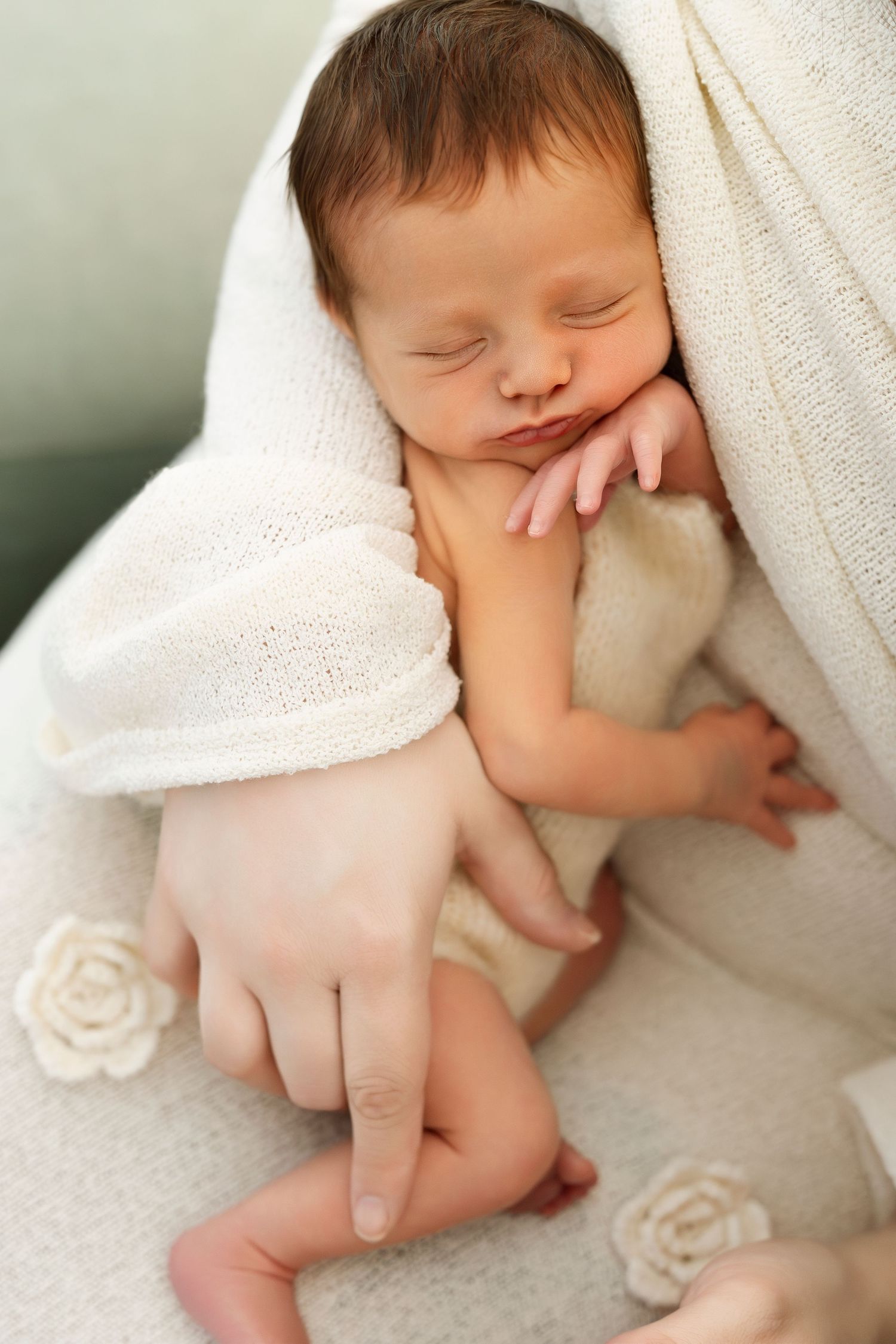 A peaceful sleeping newborn wrapped in soft white blankets with delicate rose decorations.
