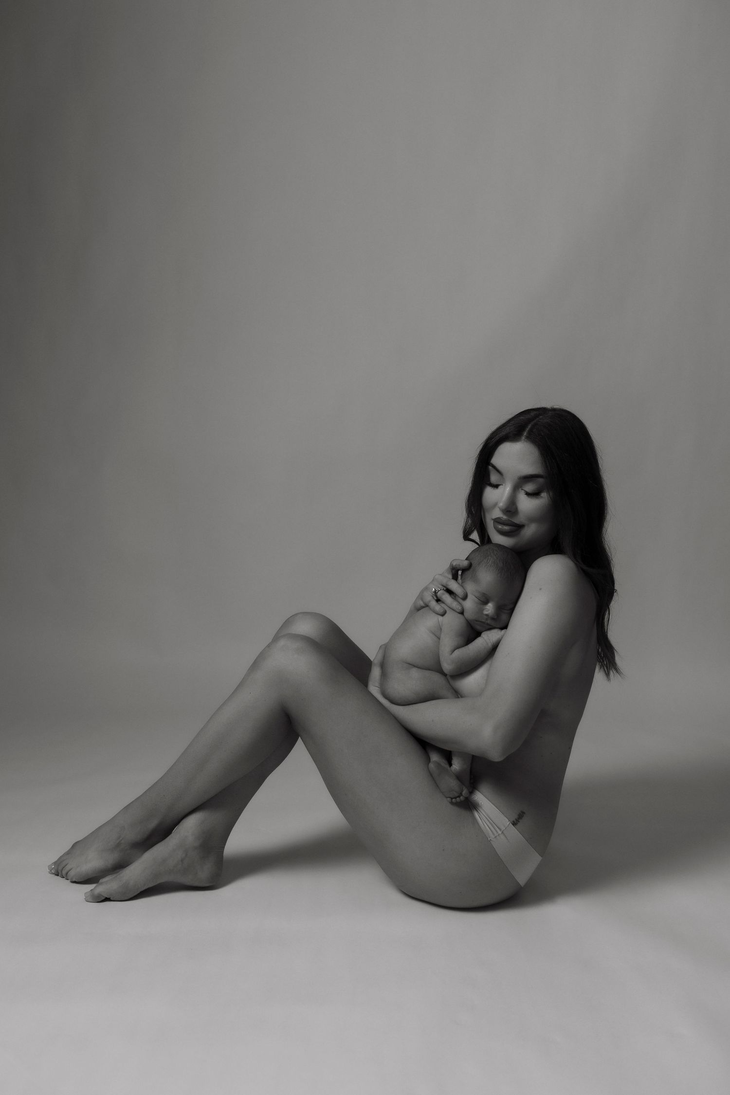 Artistic black and white nude maternity portrait on studio floor.