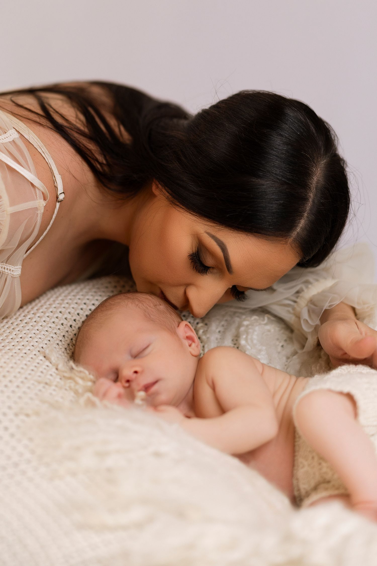 A tender moment between parent and sleeping baby on soft white knit blanket.