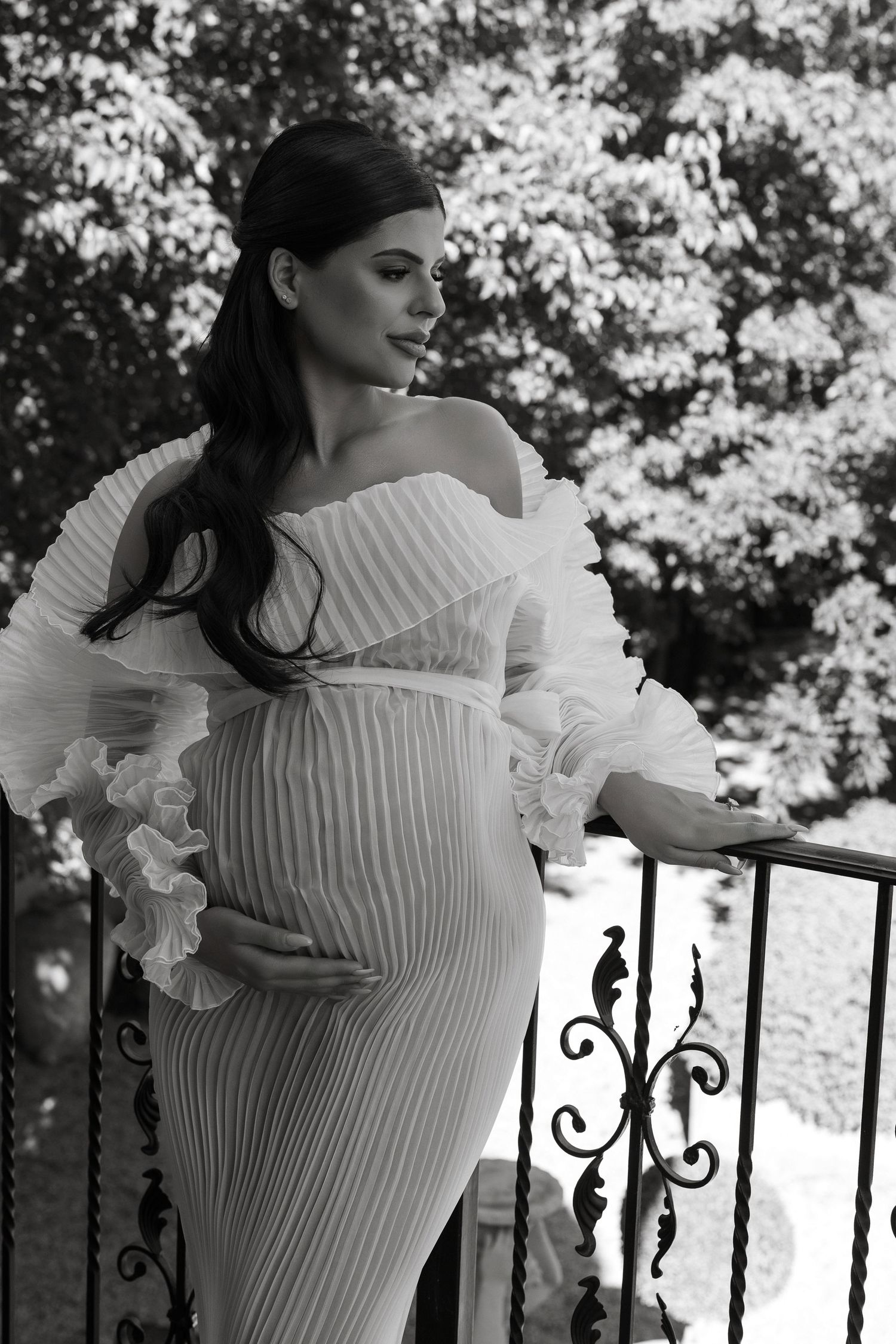 A series of black and white photos showing a woman in a white ruffled dress posing against an ornate iron railing.